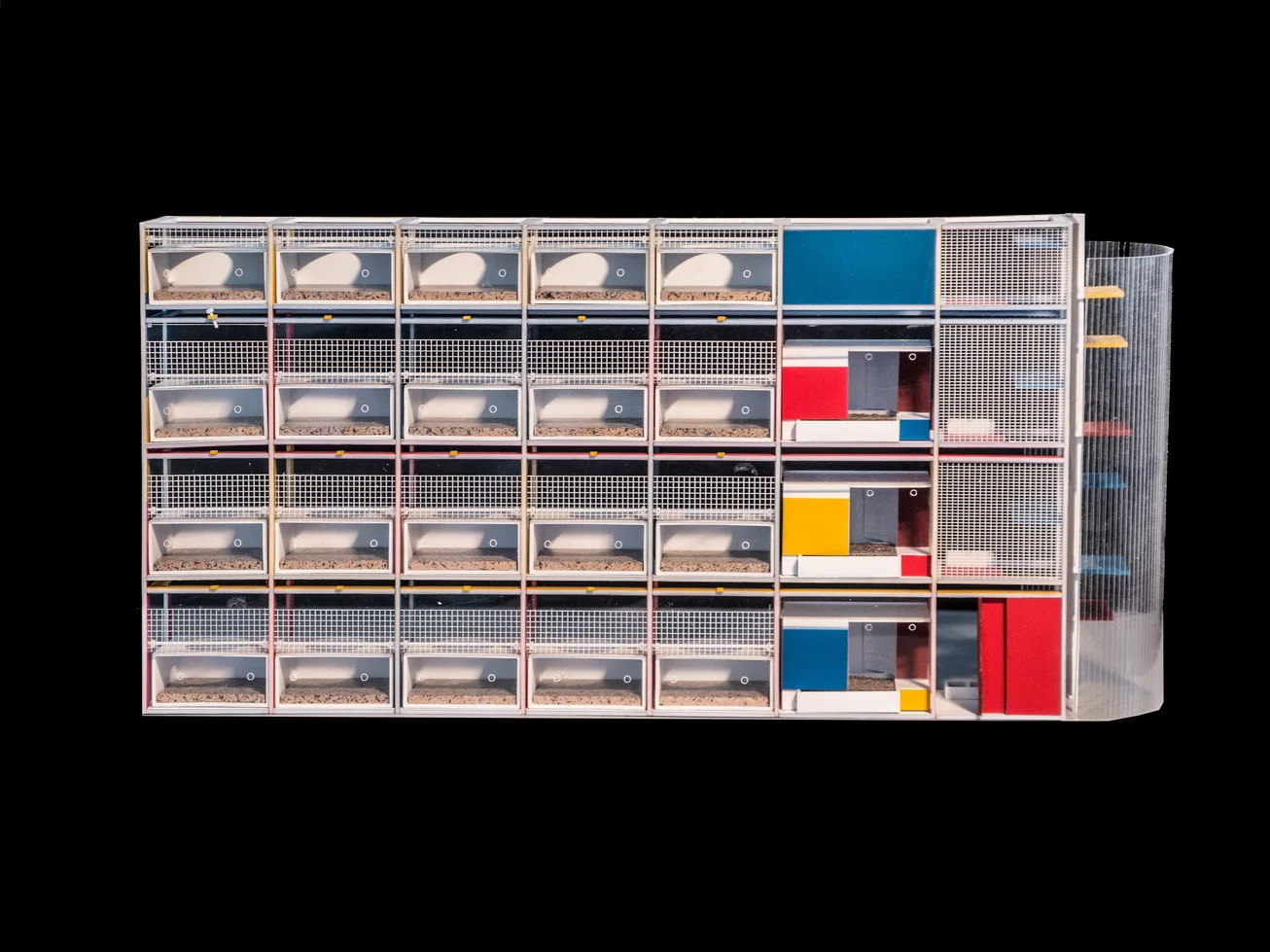 An architectural model of a white modular grid structure with red, blue, and yellow panels and metal mesh wire screens.