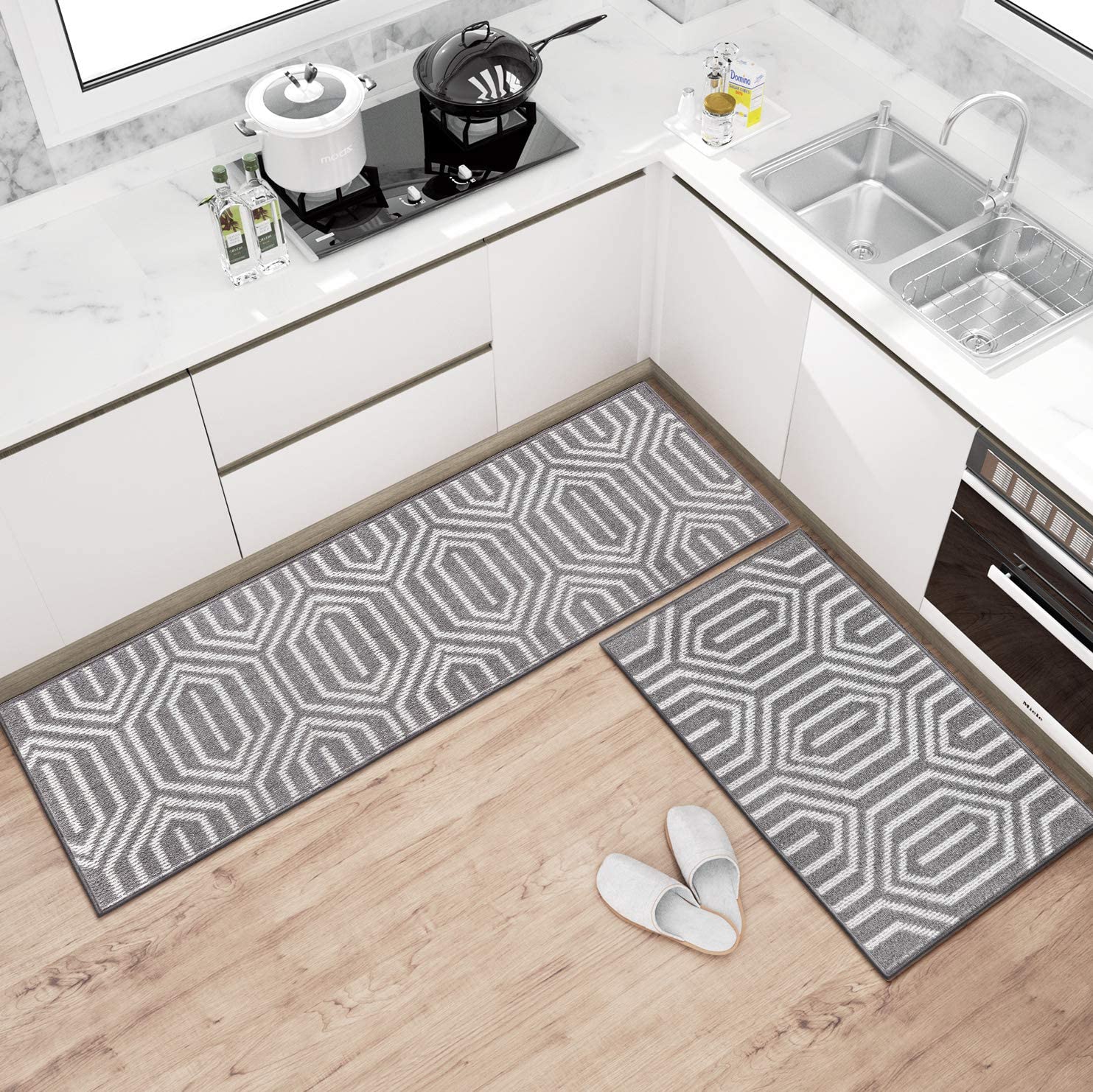 Overhead view of a white kitchen with two gray geometric runner rugs on light wood flooring next to cabinets and a stainless steel sink.