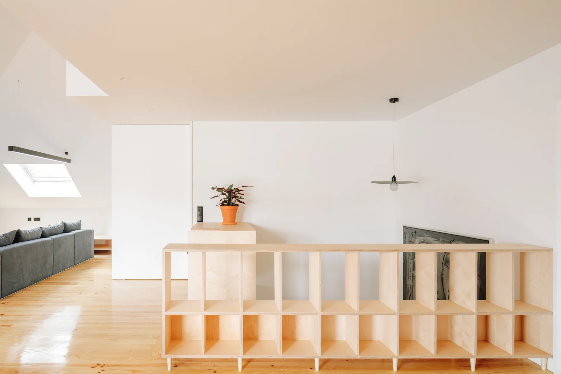 A minimalist attic living room featuring a light plywood grid shelving unit used as a partition next to a staircase.