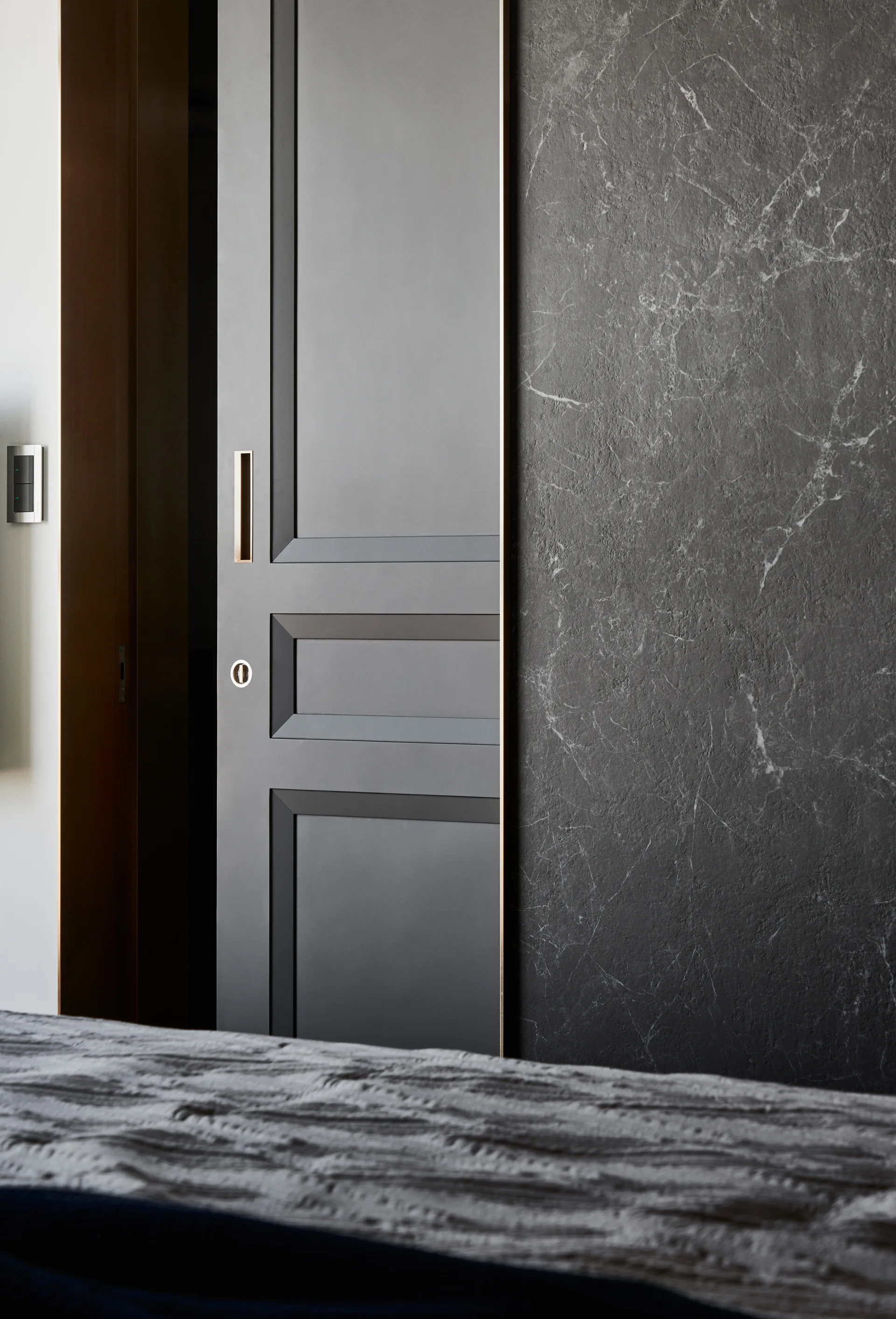 A dark charcoal sliding panel door with recessed bronze hardware sits adjacent to a veined dark stone wall.
