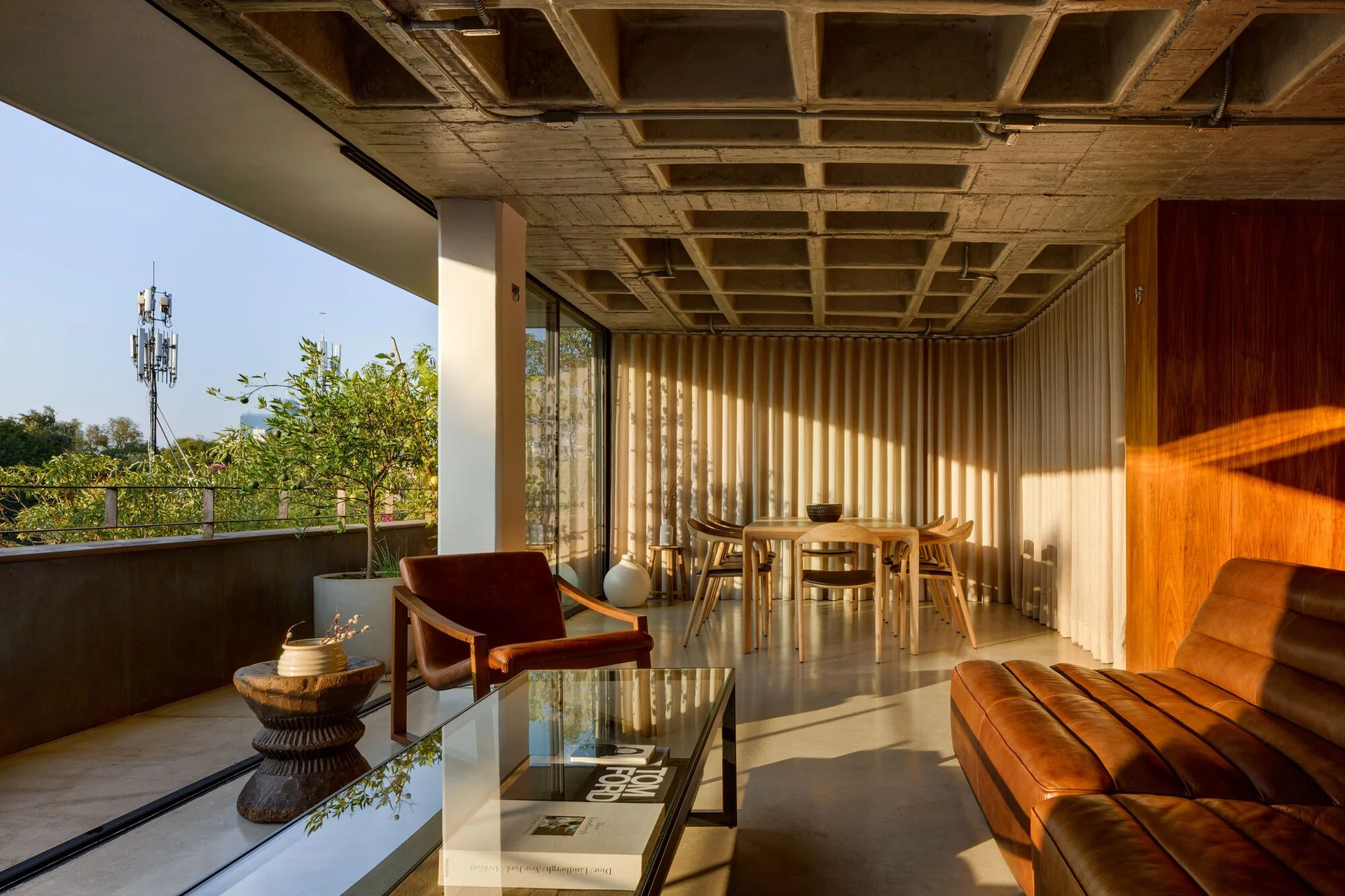 A modern open-plan living room with a concrete waffle ceiling, brown leather furniture, and sliding glass doors opening to an outdoor terrace.