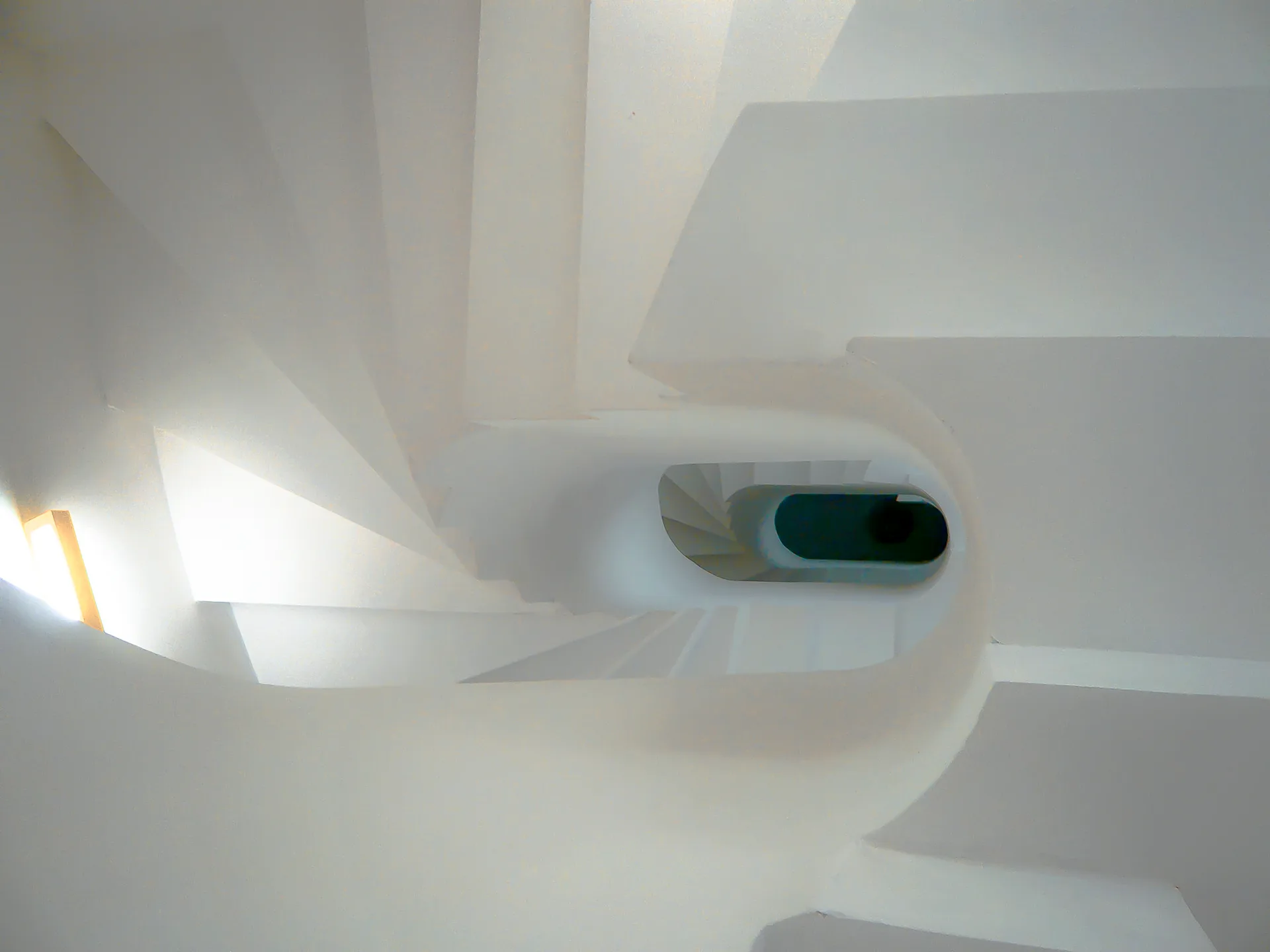 A top-down view of a modern white spiral staircase featuring smooth plaster-like steps that curve around a central dark blue void.