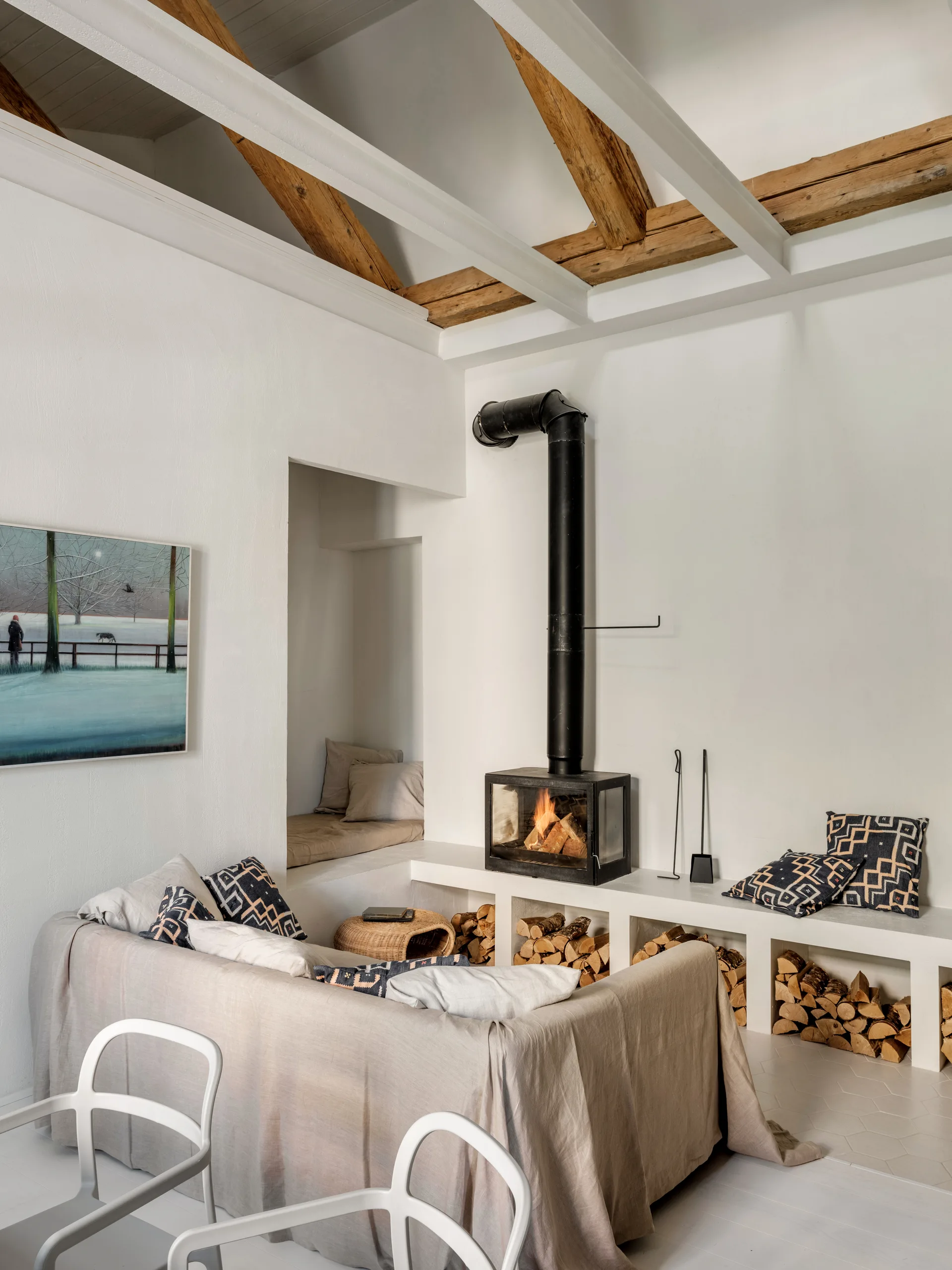A rustic living room with a black metal fireplace on a white plaster platform featuring built-in wood storage underneath.