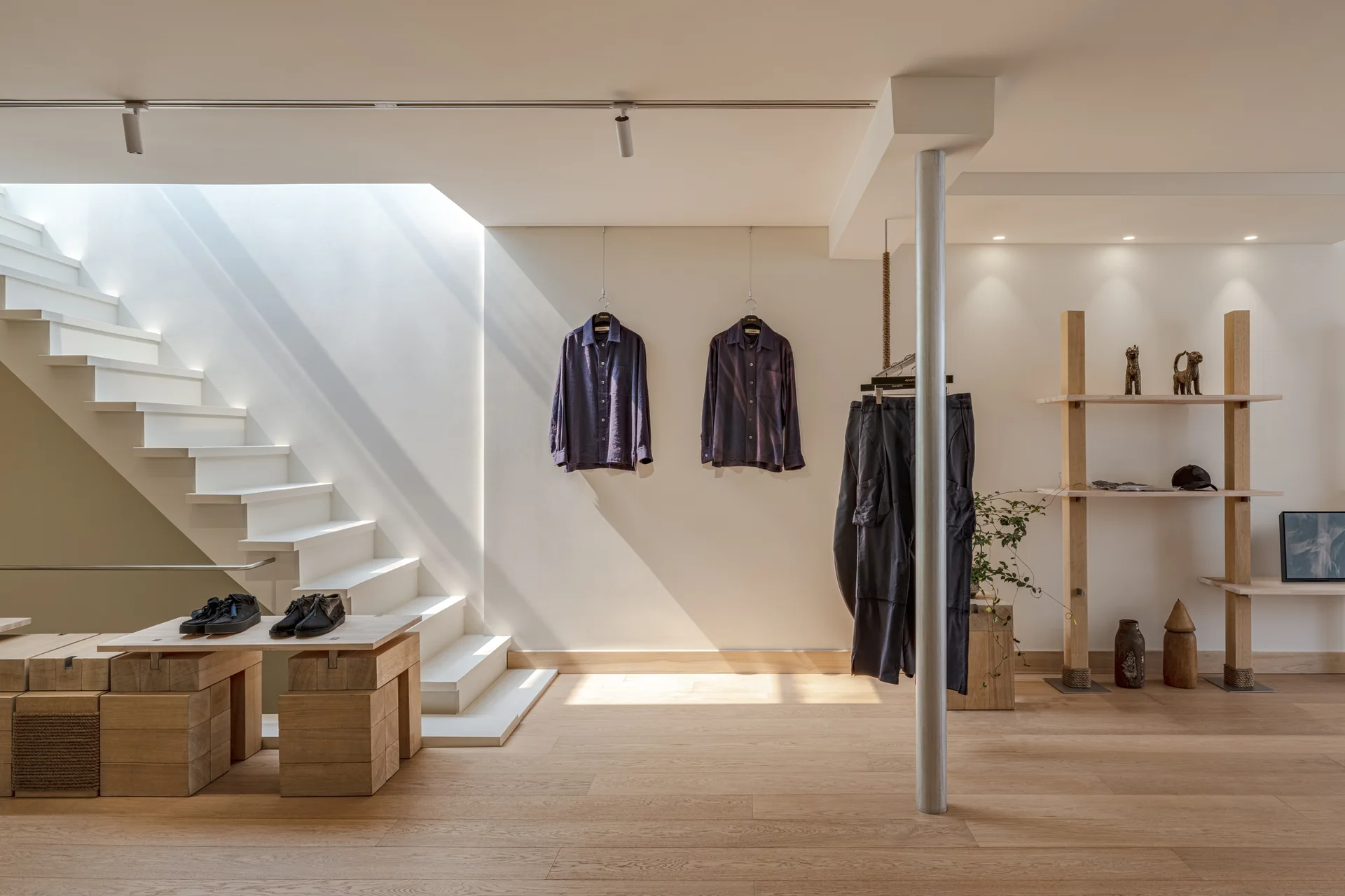 A minimalist retail space features a white floating staircase, light wood floors, modular wooden display blocks, and wooden shelving.