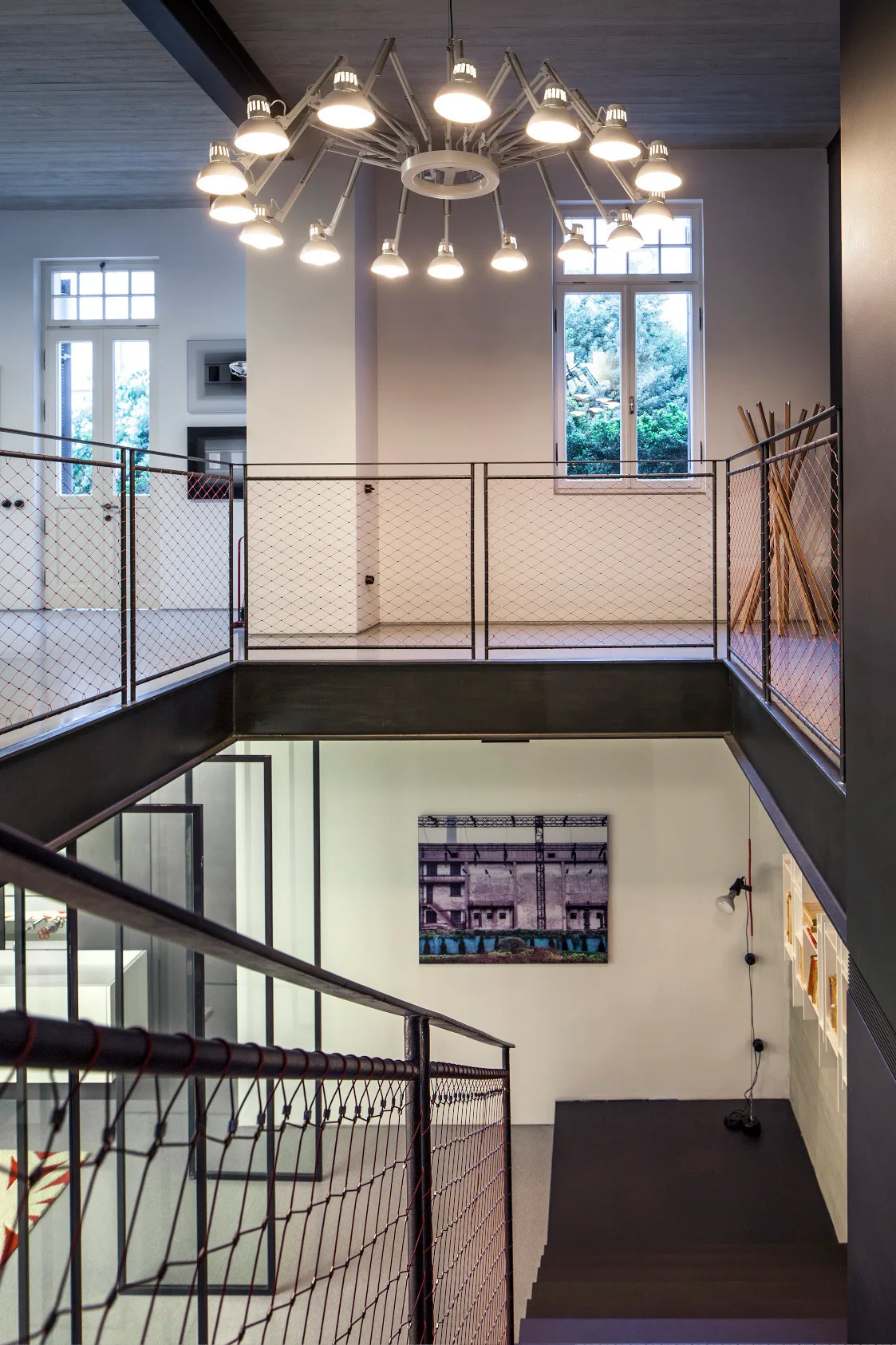 An industrial steel staircase and landing feature black metal railings with mesh panels under a large multi-arm articulated chandelier.