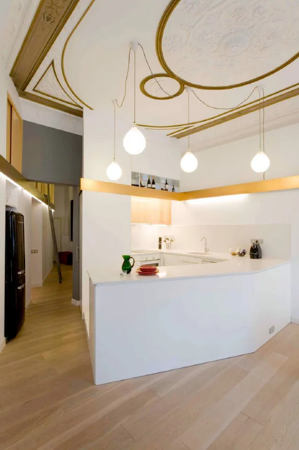 A modern white u-shaped kitchen with spherical pendant lights beneath an ornate white ceiling with decorative gold moulding.