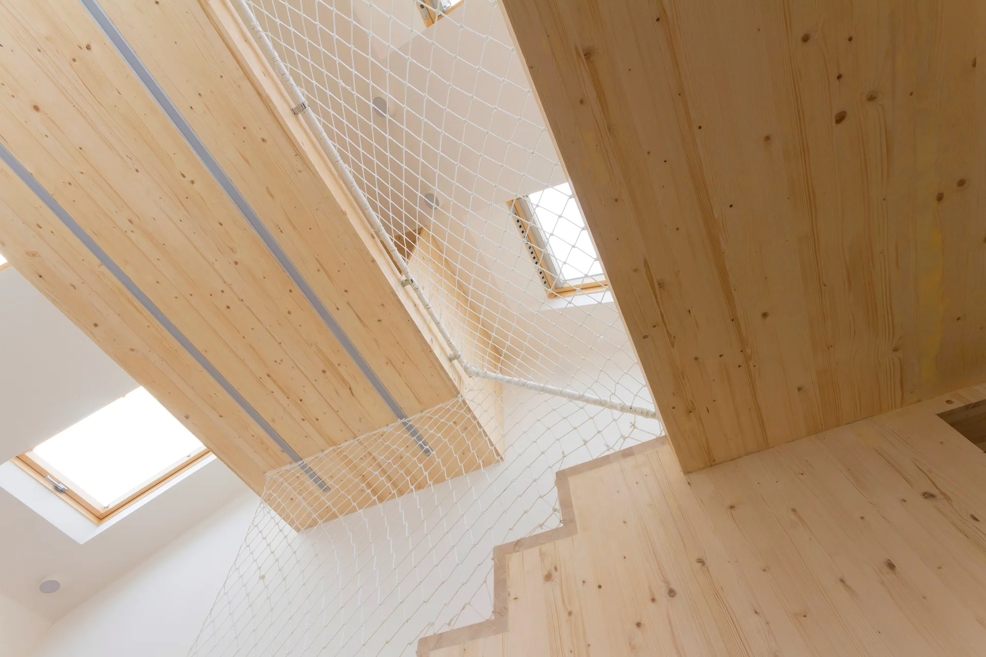 A light wood staircase and mezzanine are enclosed by white rope safety netting under bright skylights.