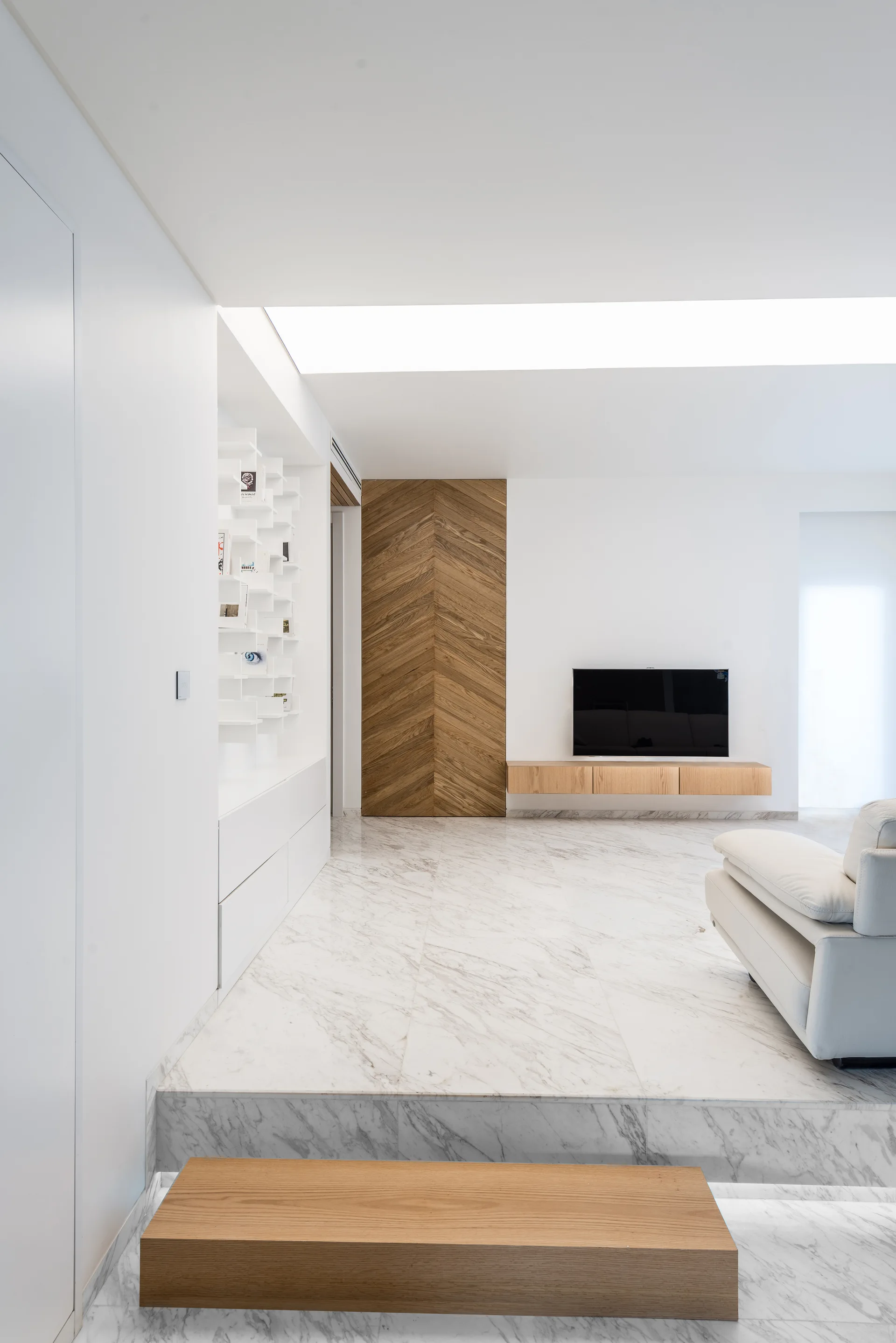A contemporary living room featuring white marble tile flooring, a chevron-patterned wood accent wall, a floating media console, and a white sofa.