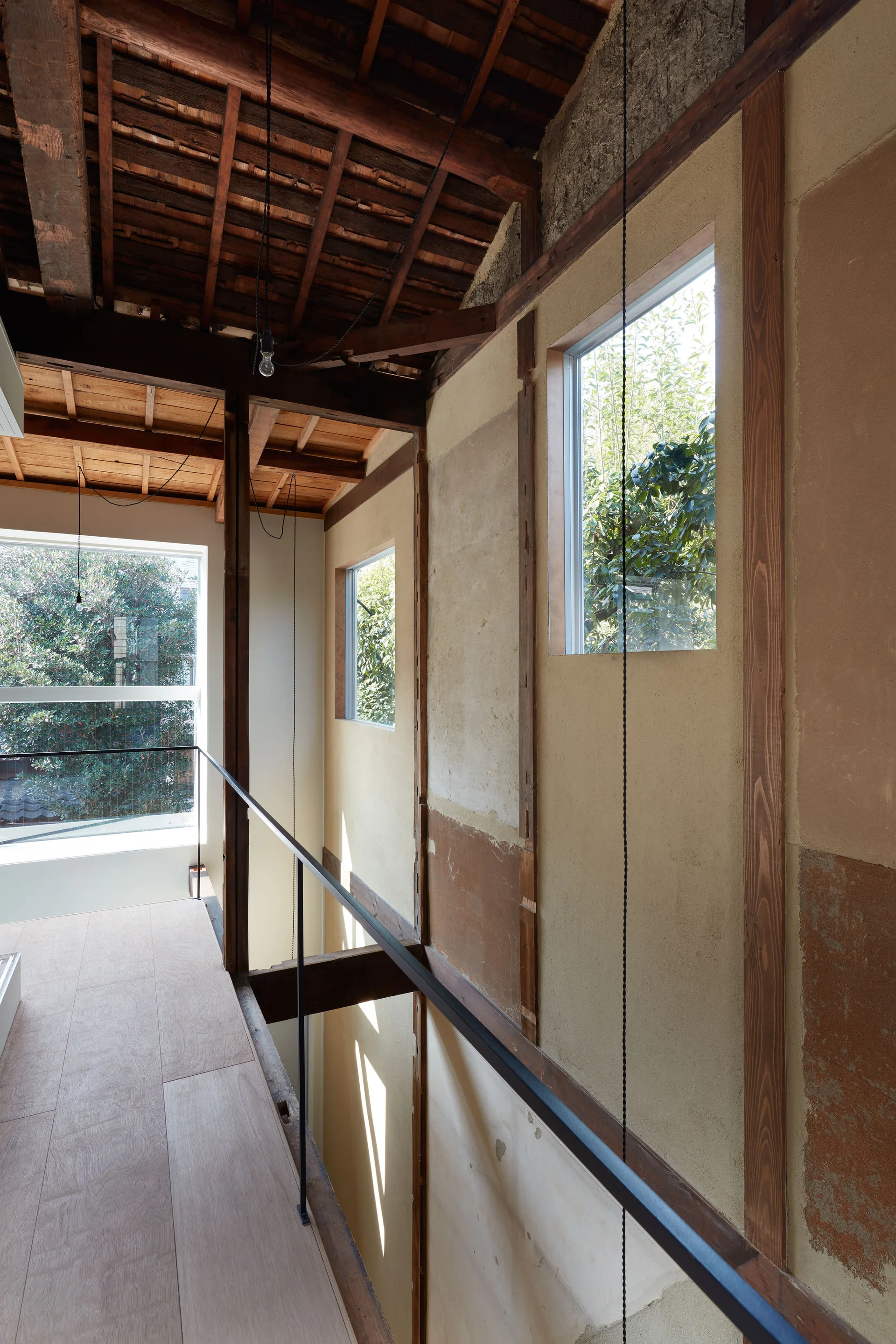 A light wood landing features a black metal railing, textured plaster walls with timber framing, and an exposed dark wood roof structure.