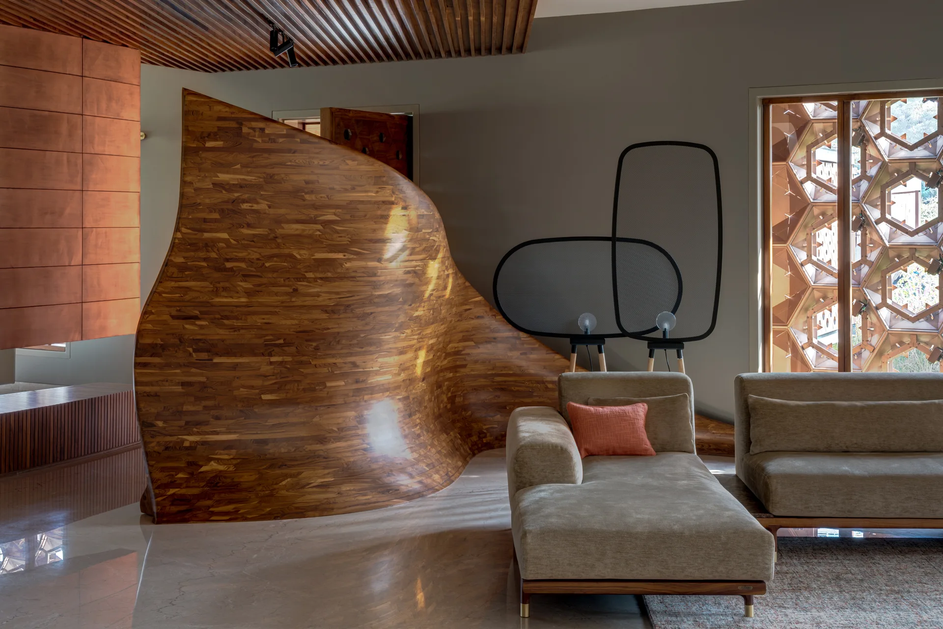 A contemporary living room featuring a large wave-shaped wood room divider, tan upholstered sofas, and a linear slatted ceiling.