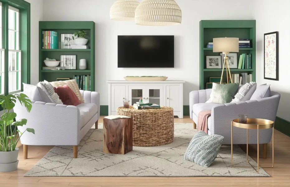 Two light grey sofas face each other in a bright living room with dark green built-in bookshelves and a woven coffee table.