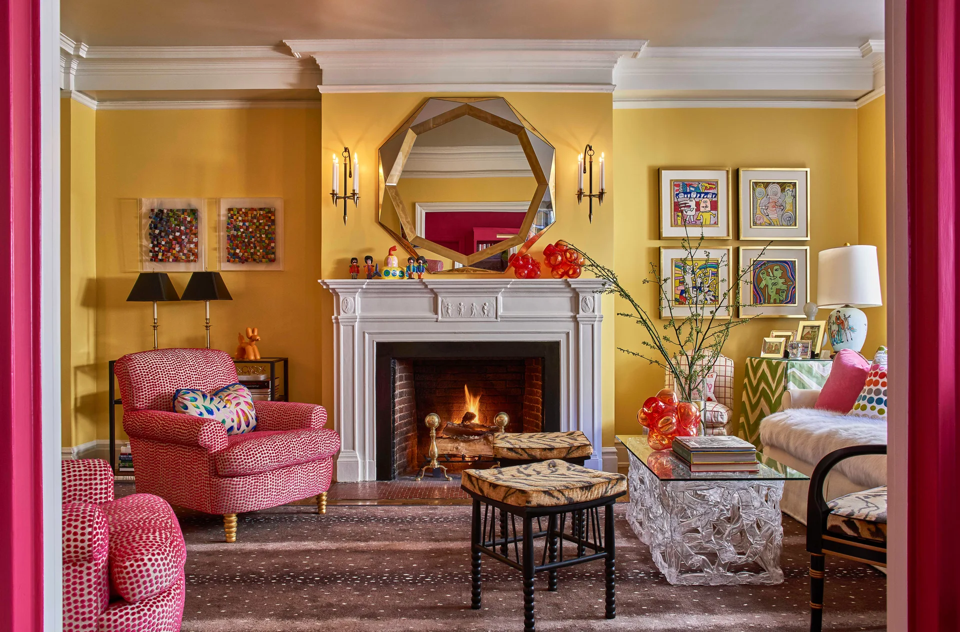 A yellow living room features a white fireplace mantle, a geometric gold mirror, pink patterned armchairs, and tiger-print stools.