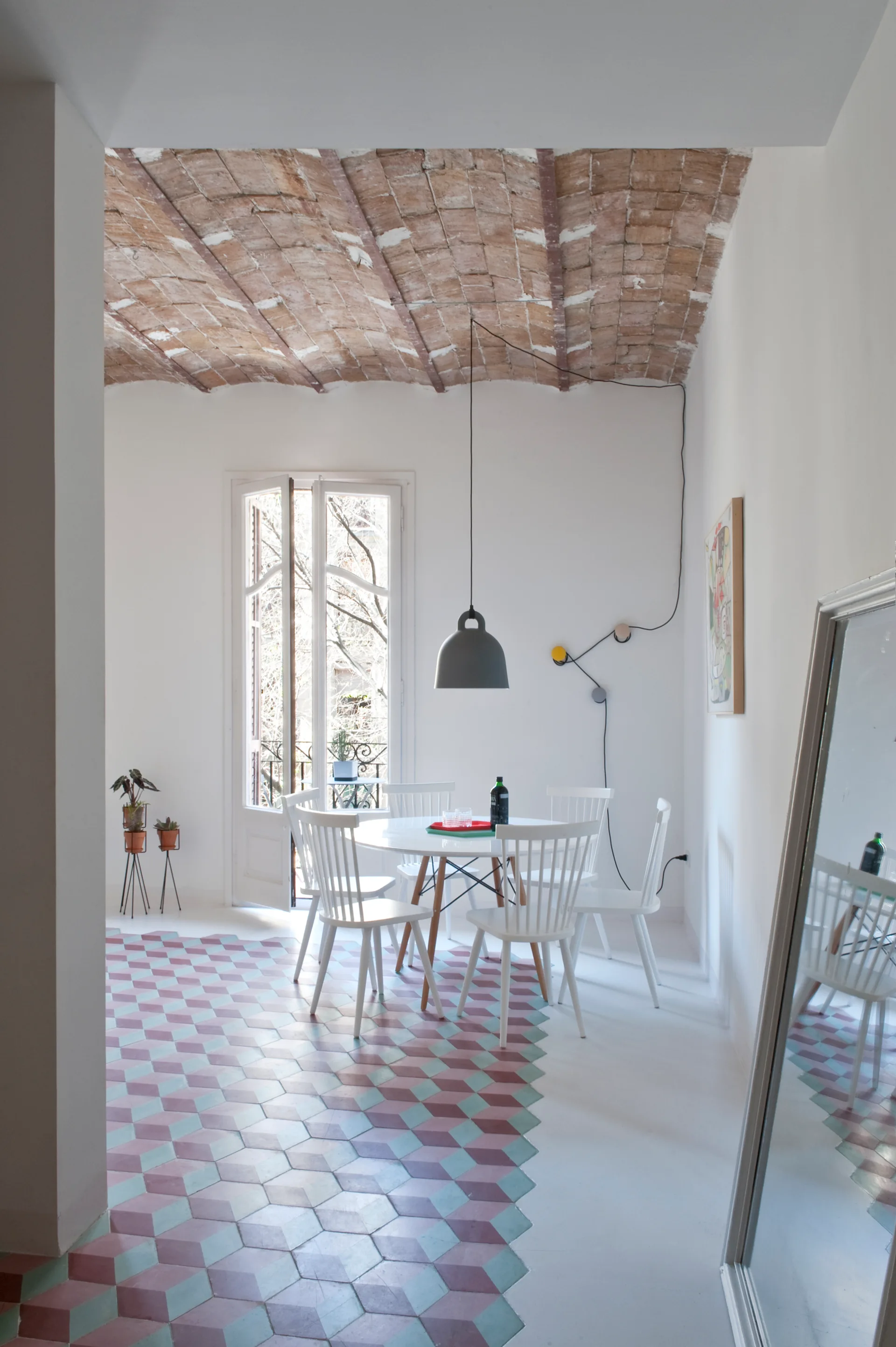 A bright dining room features a white round table and spindle chairs, geometric floor tiles, and an arched terracotta brick ceiling.