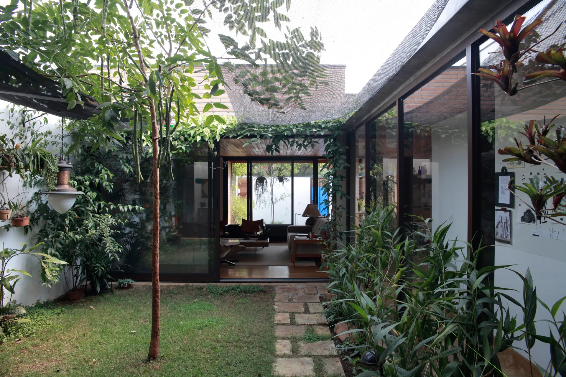 A lush courtyard garden features a stone pathway leading toward large sliding glass doors that open into a modern wood-ceilinged living space.