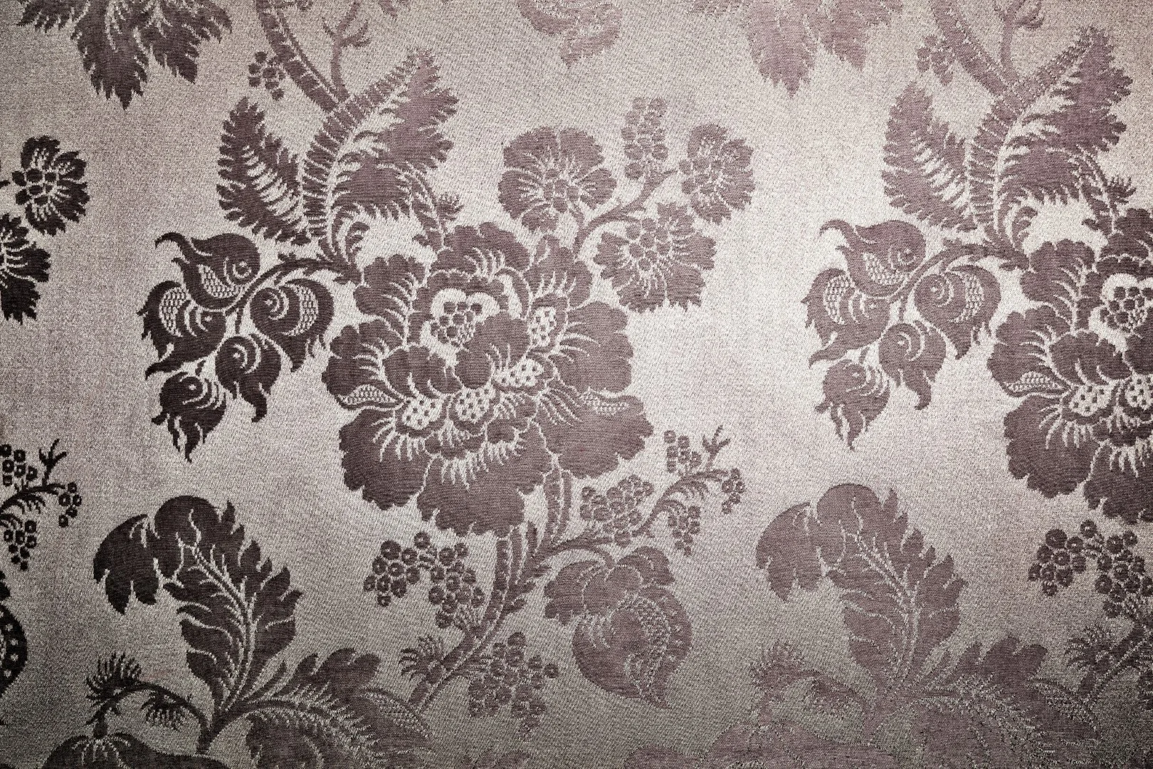 Close-up of a grey and taupe jacquard woven fabric showing an intricate traditional floral damask pattern with raised texture.