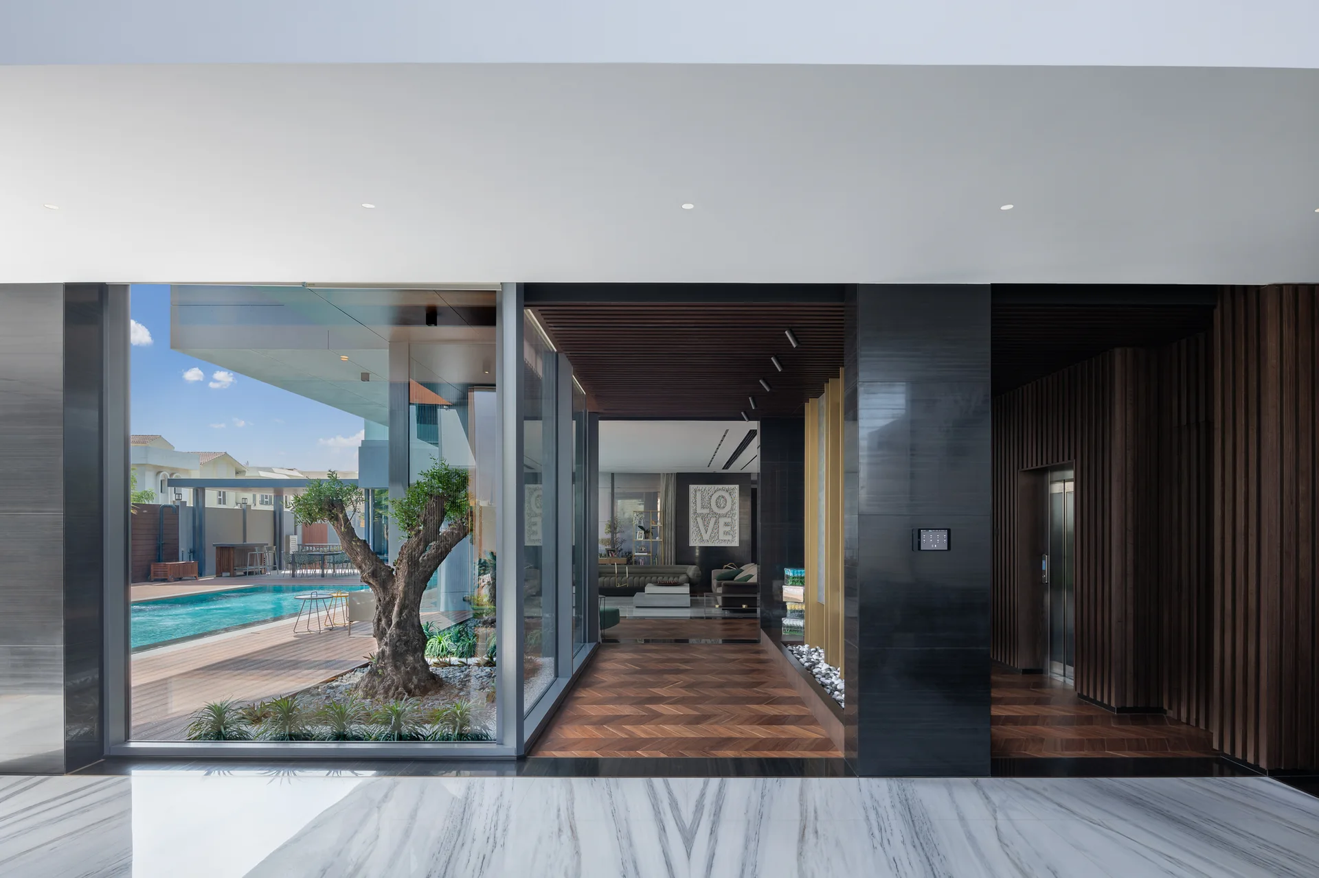 Modern entryway featuring herringbone wood flooring, dark stone walls, and a glass wall looking out to an indoor courtyard tree and outdoor pool.