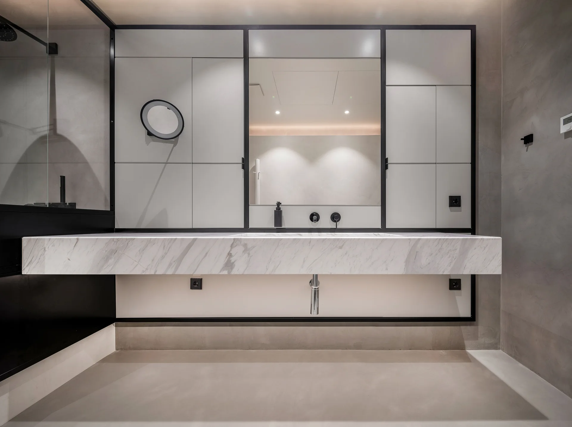 A modern bathroom features a thick floating marble vanity beneath a mirrored wall system bordered by light grey cabinets and thin black metal trim.