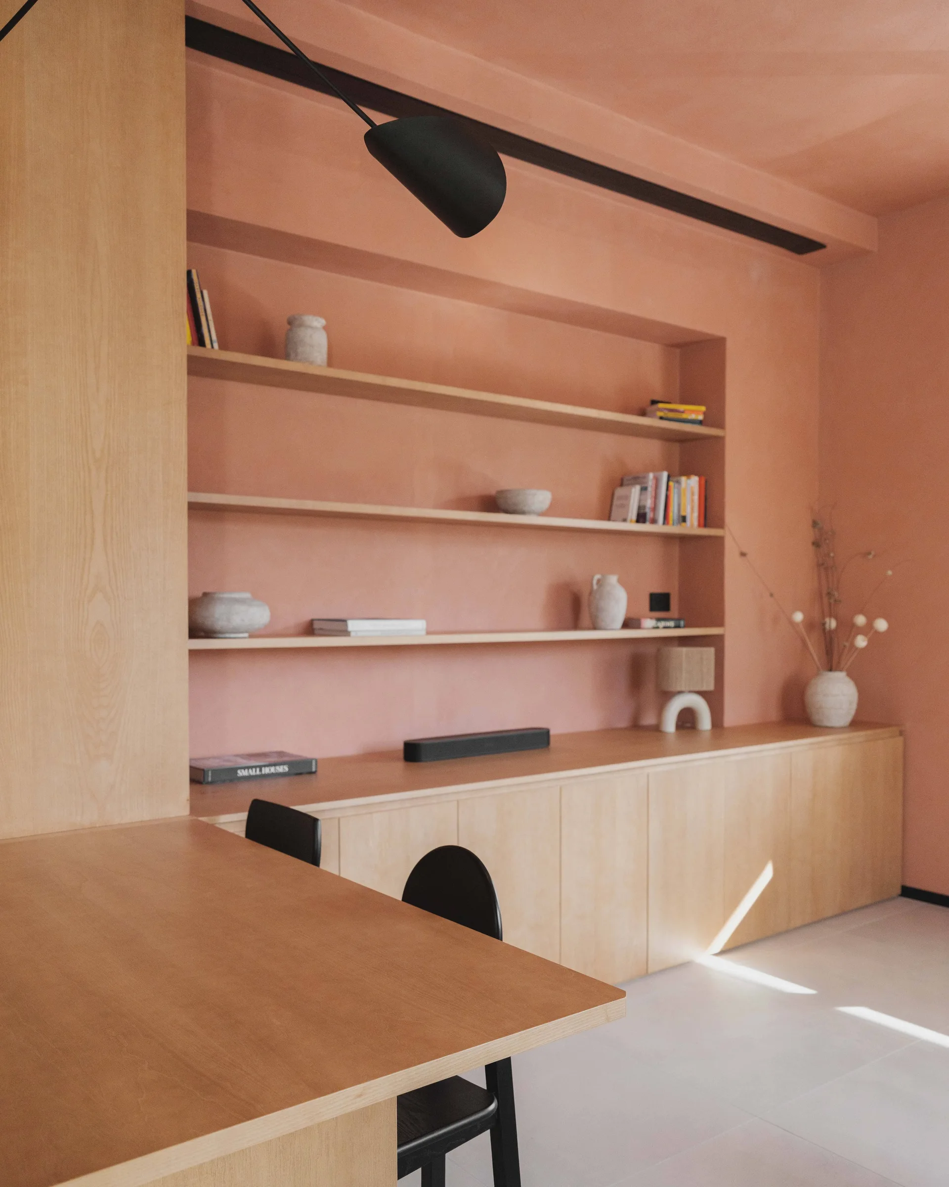 A minimalist room featuring matte terra-cotta plaster walls and ceiling with a custom light wood storage unit and recessed shelving.