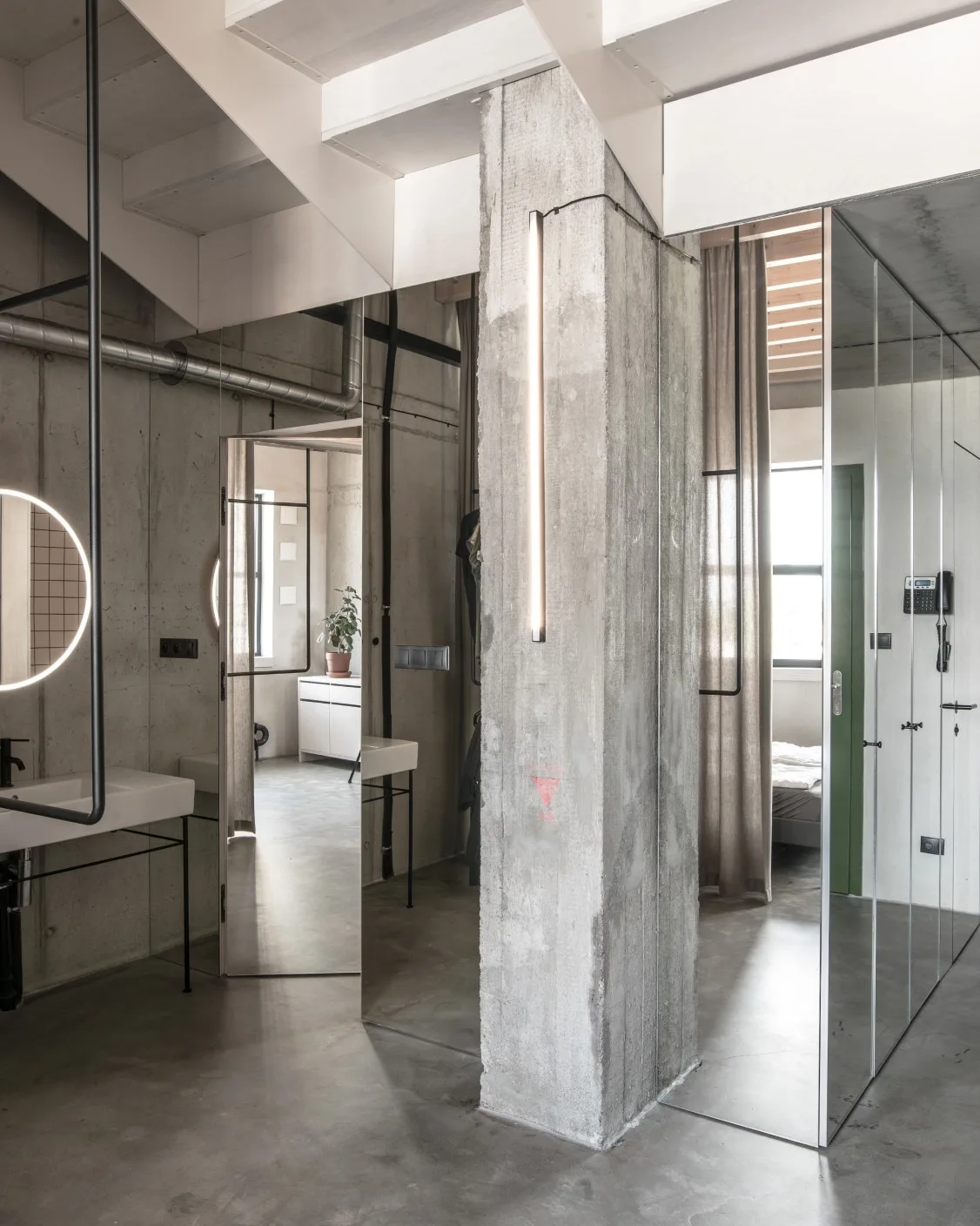 An industrial loft bathroom with raw concrete walls, a structural pillar, and large mirrored partition panels.
