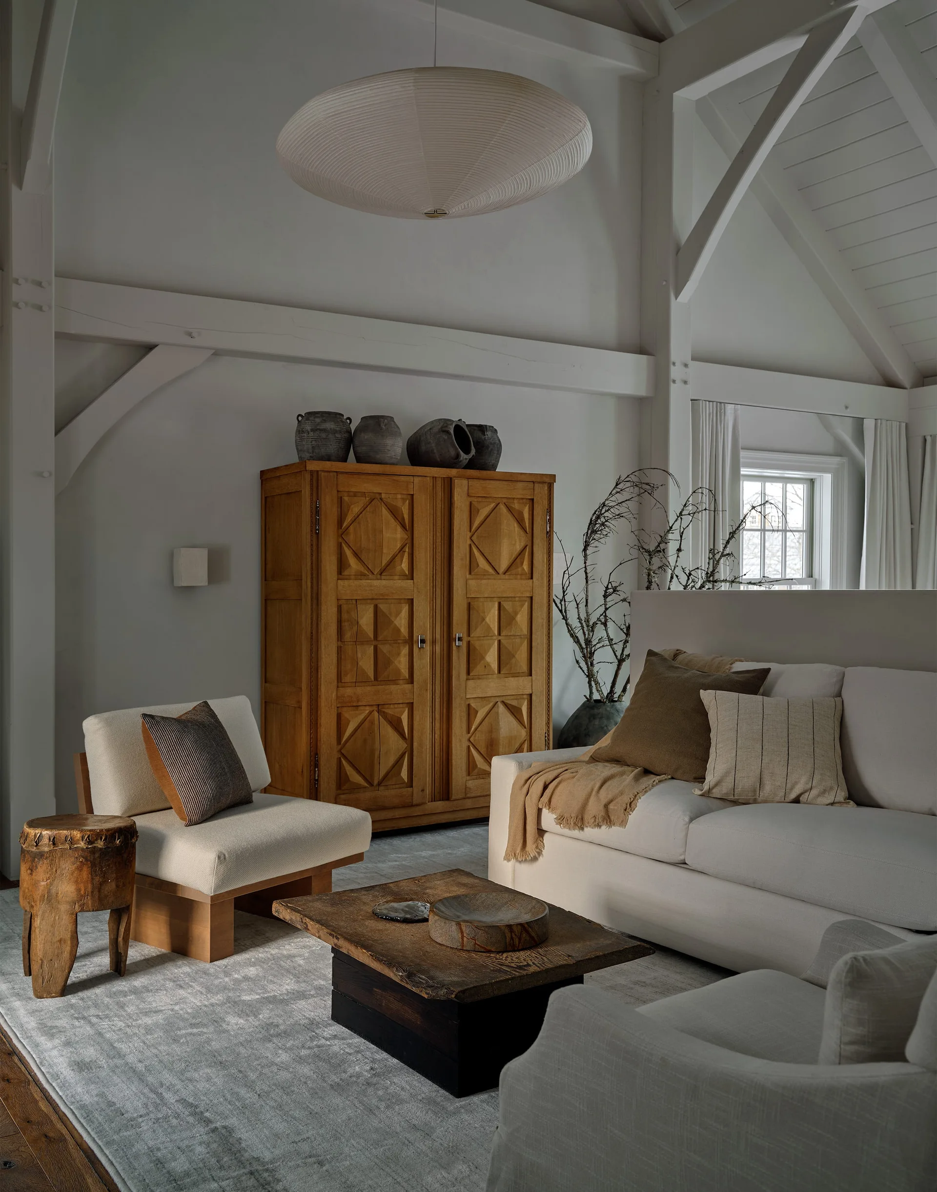 An organic modern living room featuring white vaulted ceilings, a geometric wood cabinet, neutral sofas, and a rustic coffee table.