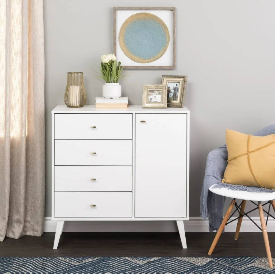 A white mid-century modern dresser sits next to a chair with a mustard yellow pillow, on a dark wood floor with a blue chevron rug.