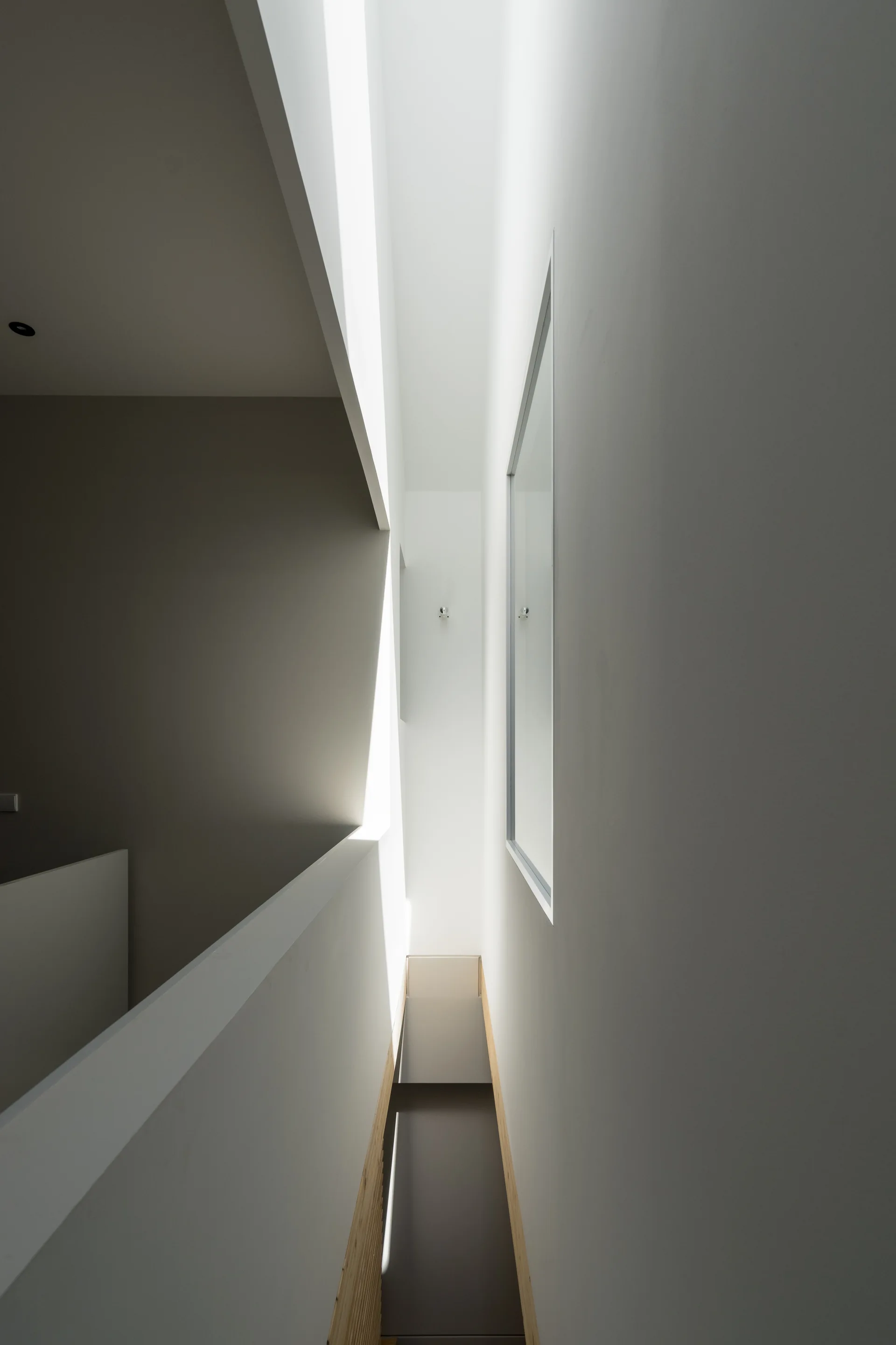 A minimalist white staircase corridor features a high vertical light well, smooth plaster walls, and a clean geometric railing.