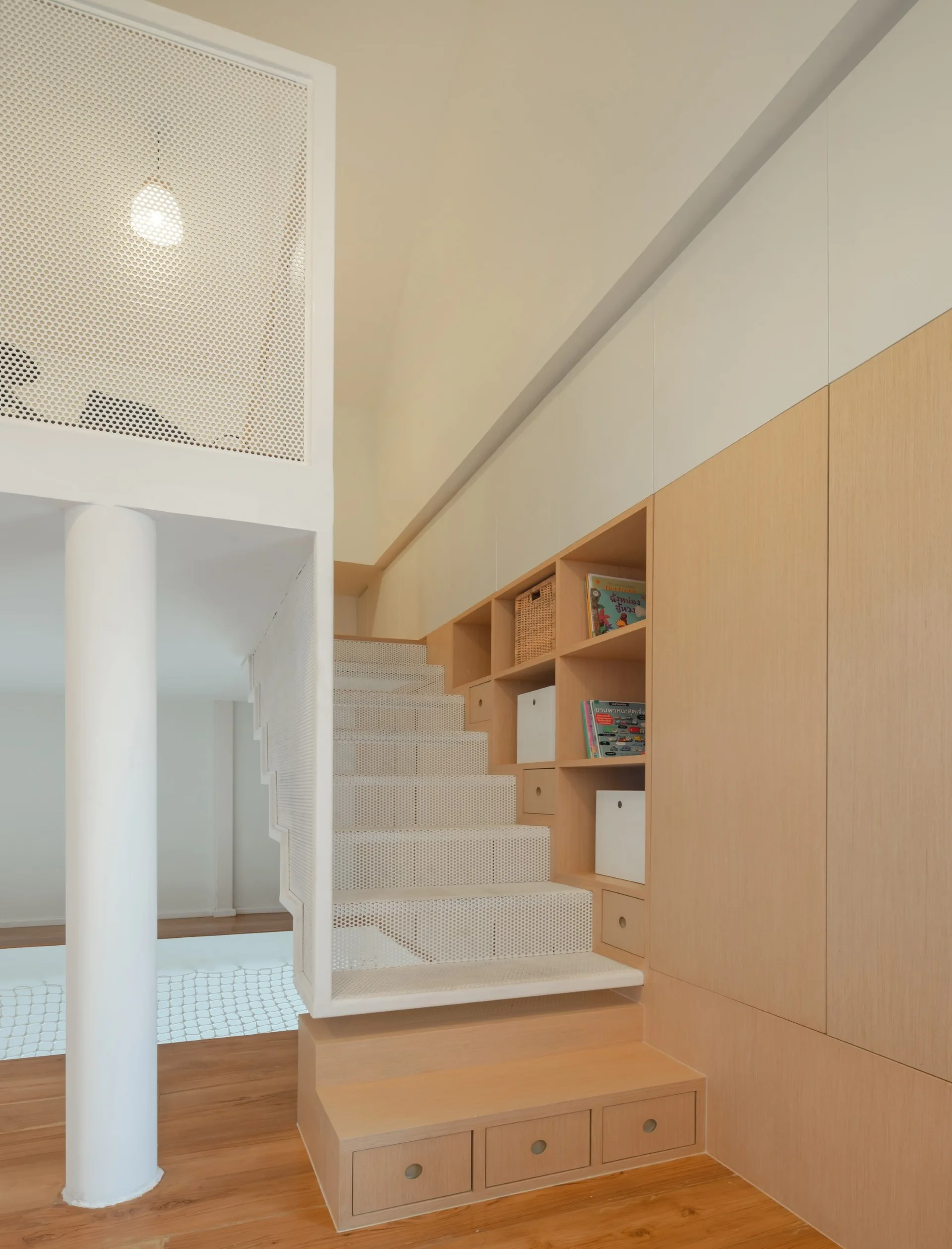 A modern white perforated metal staircase integrated with a wall of light-toned wood cabinets and open storage shelves.
