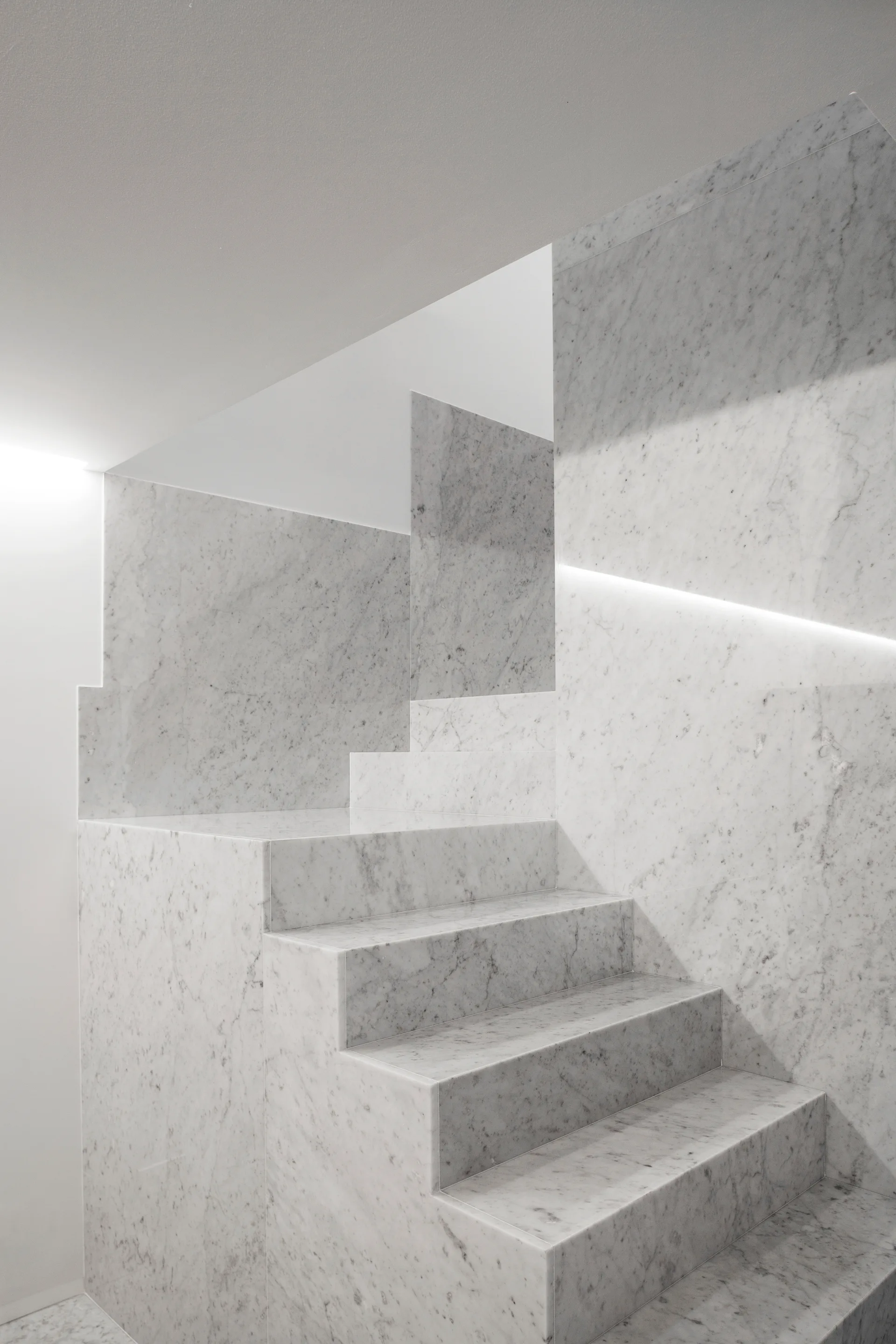 A minimalist staircase crafted from polished white marble featuring integrated LED strip lighting along the wall.