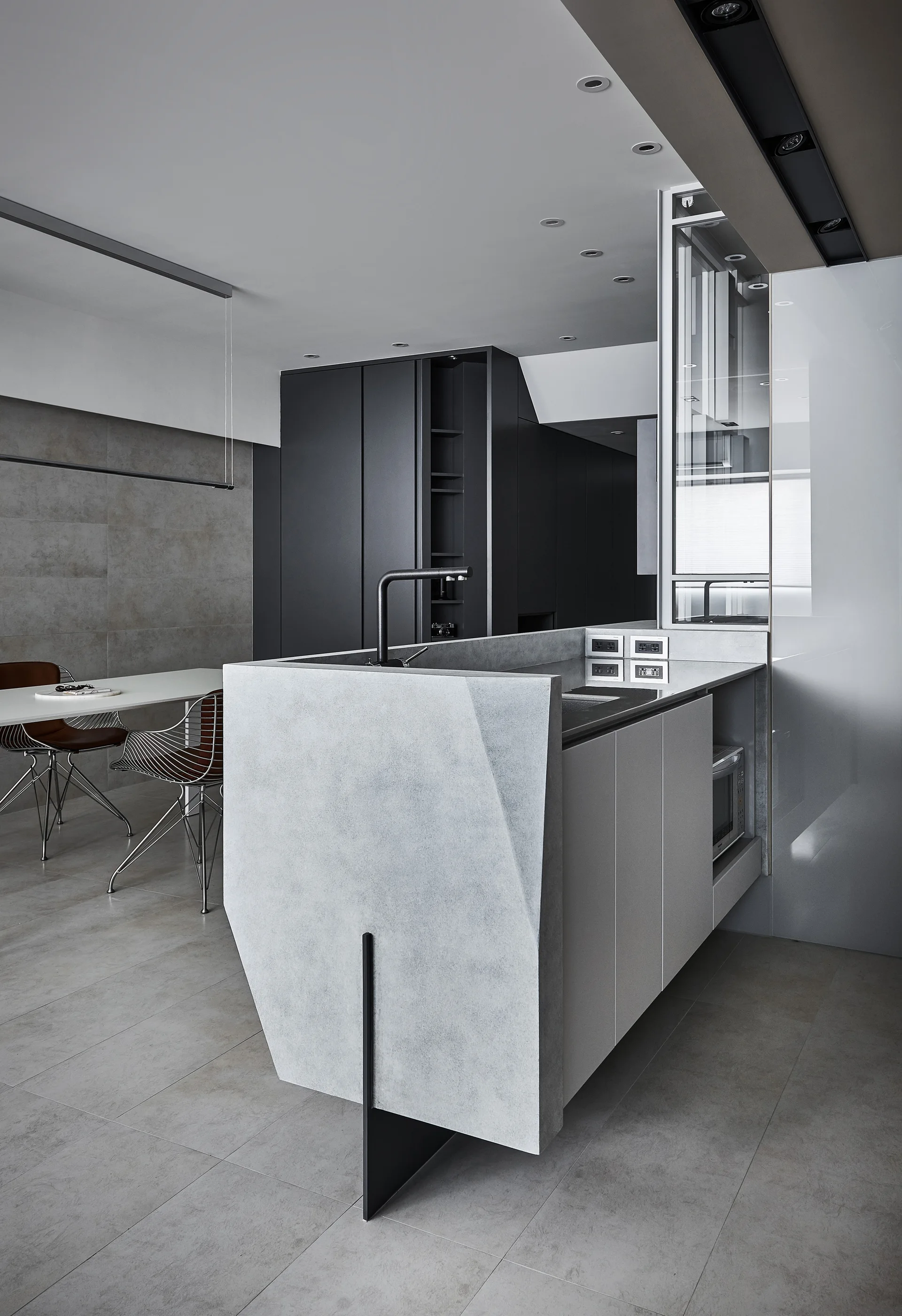 A modern minimalist kitchen features a sculpted gray stone-like island with a black faucet, built-in microwave, and dark cabinetry in the background.