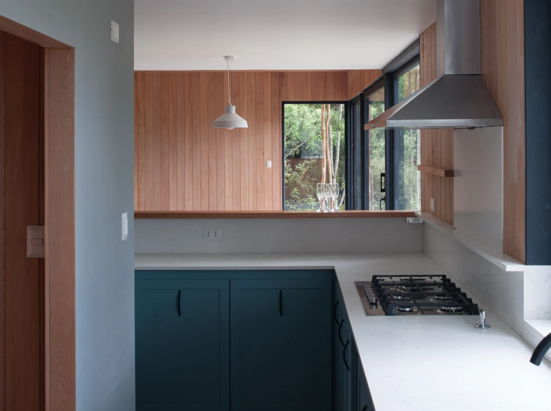 A kitchen featuring dark teal lower cabinets, white stone countertops with a gas cooktop, and warm vertical wood paneling on the walls.