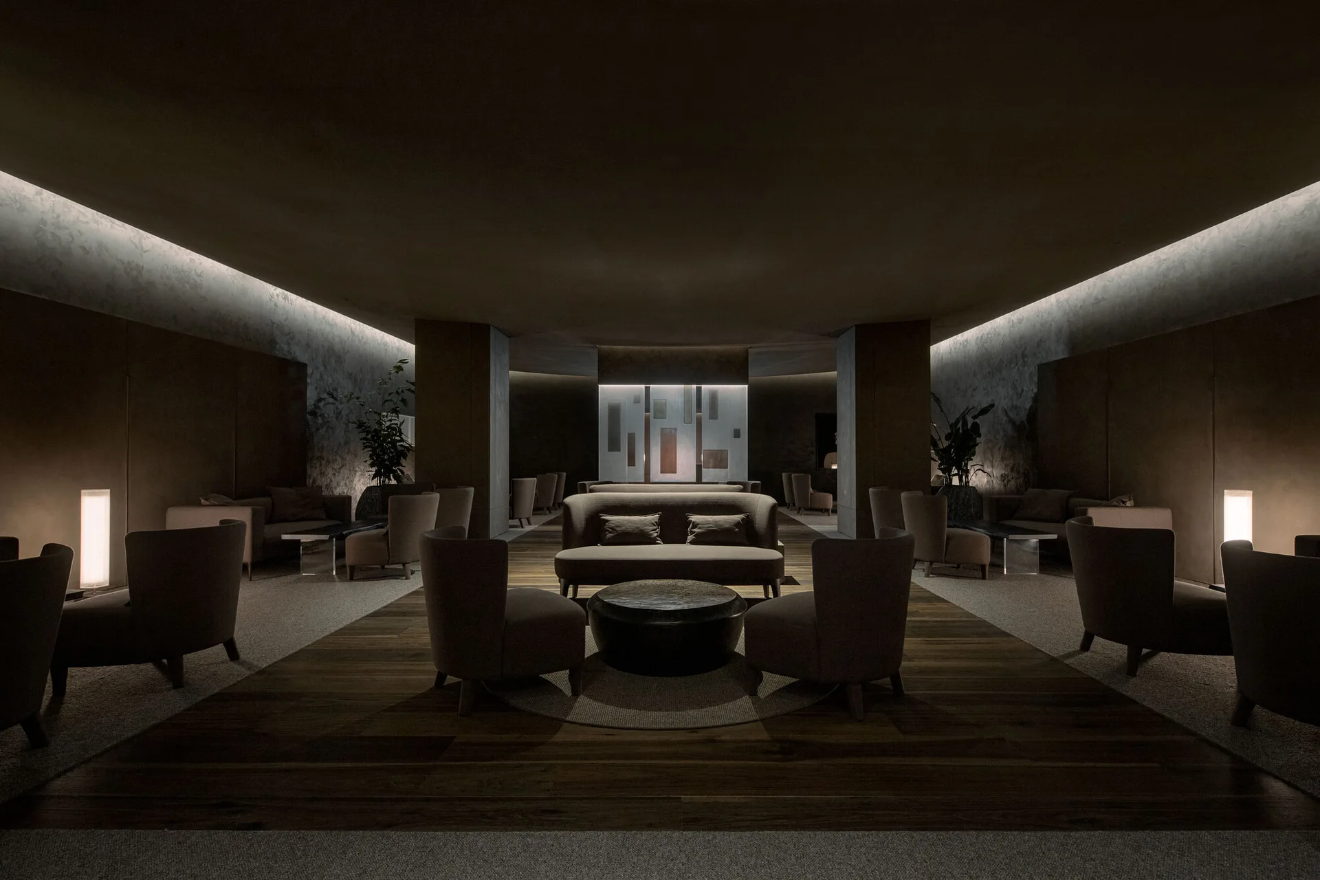 Symmetrical lounge interior featuring brown armchairs, a central sofa, glowing cove lighting, and a dark wood floor inlay.