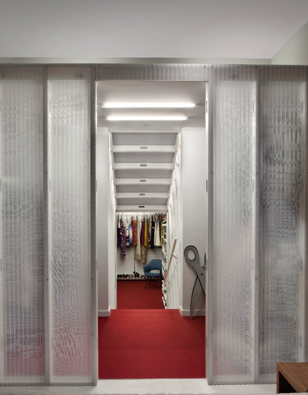 A walk-in closet with bright red carpeting and hanging clothes is visible through opened translucent corrugated sliding partition panels.