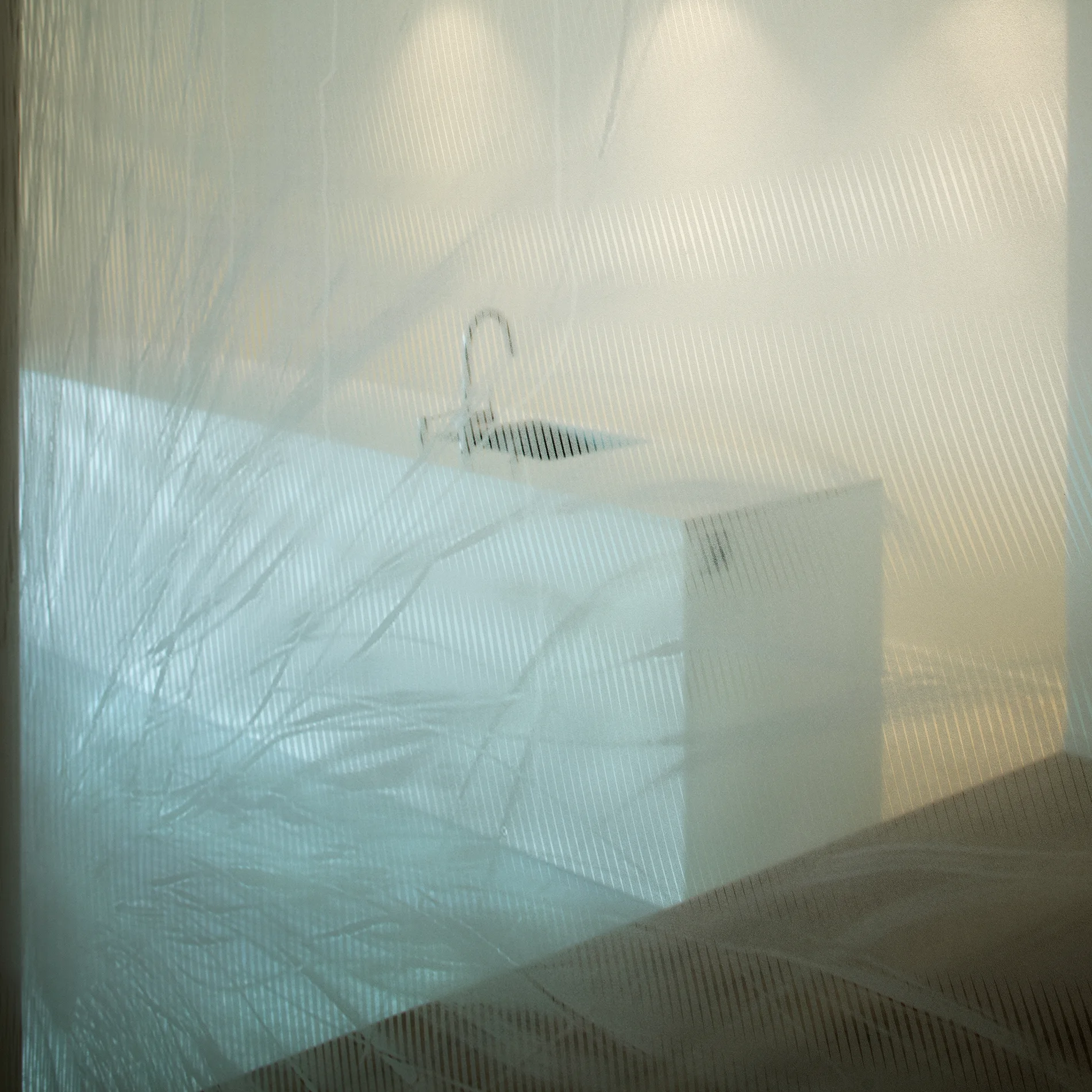A minimalist white kitchen island and chrome faucet are viewed through a semi-transparent, striped glass screen under soft lighting.