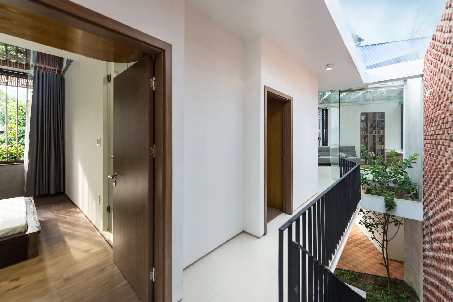 A bright white hallway featuring wood-framed doorways, a black metal railing, and a view into an open-air brick atrium.