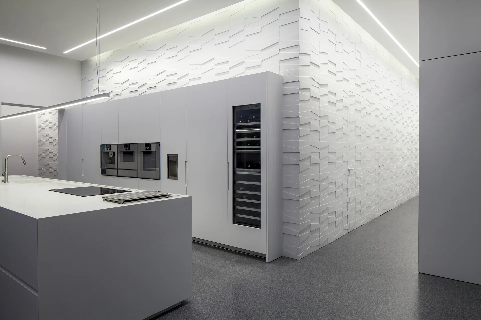 A minimalist kitchen features seamless white cabinetry with integrated appliances, a central island, and a textured geometric wall.