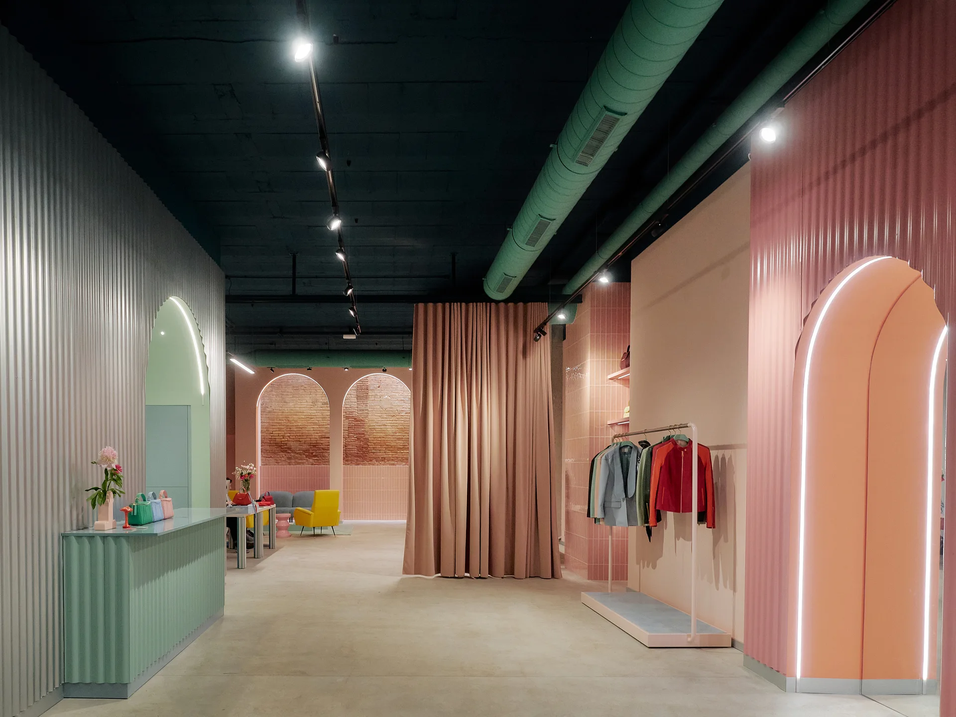A spacious retail interior features pastel pink and green corrugated walls, arched portals, a mint green reception desk, and a dark exposed ceiling.