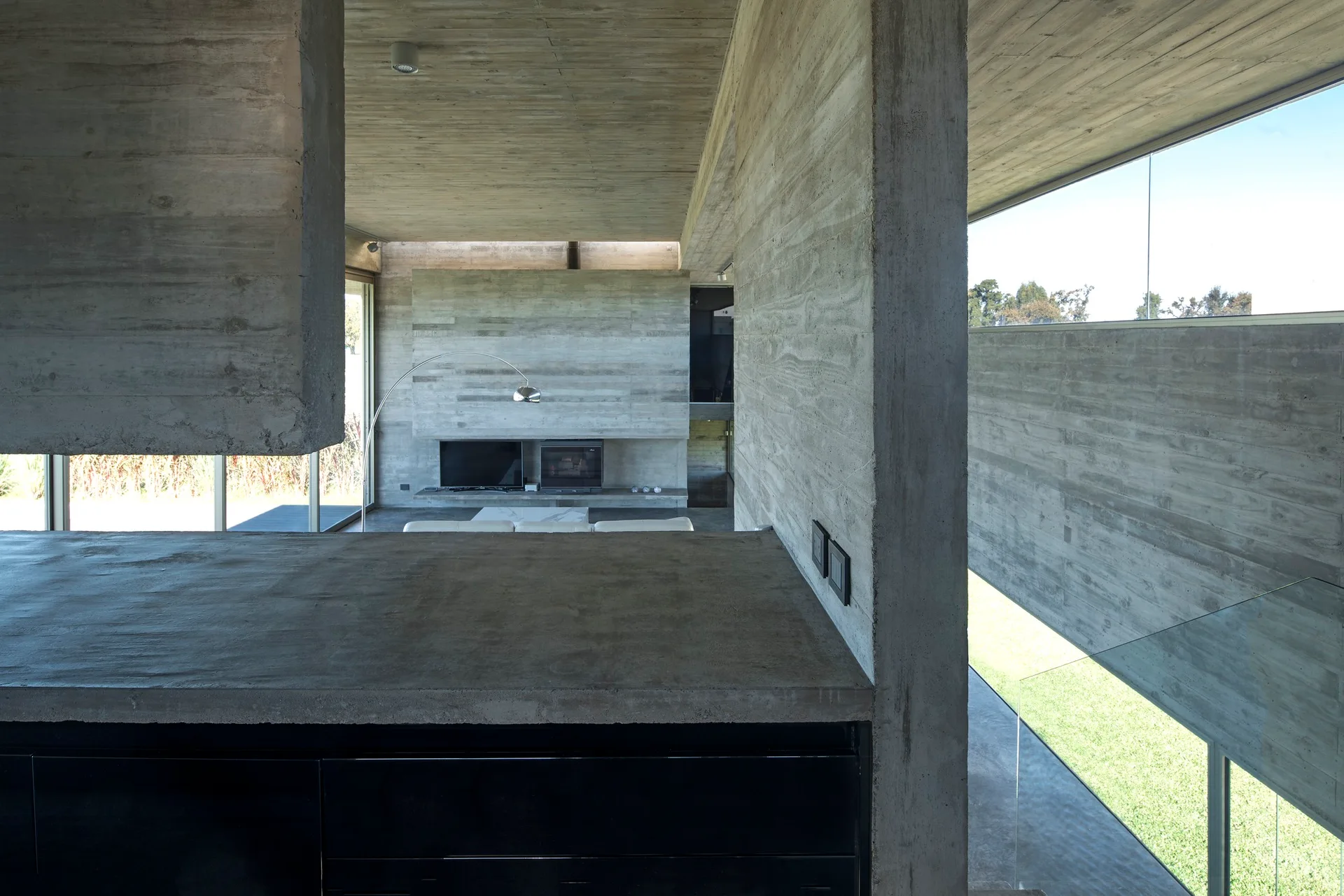 A minimalist home interior with raw board-formed concrete walls, a concrete ceiling, large horizontal windows, and a modern living area in the background.