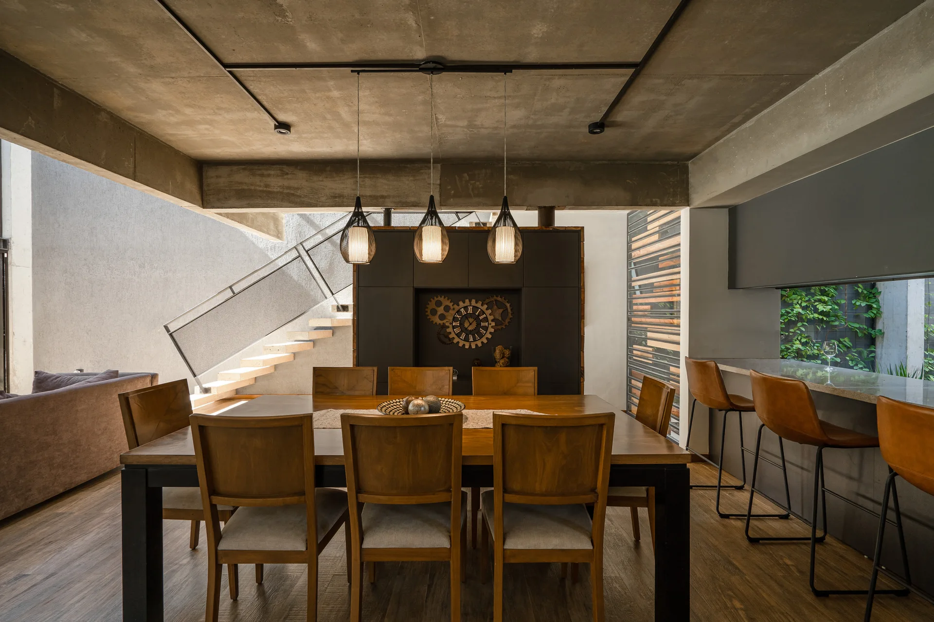 A modern dining room featuring a wooden table with chairs under industrial pendant lights and an exposed concrete ceiling.