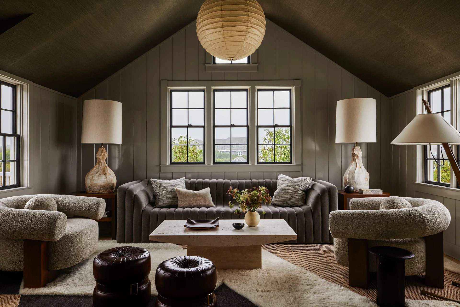 Symmetrical living room featuring a grey channel-tufted sofa, cream boucl%%e armchairs, a travertine coffee table, and a paper globe pendant light.