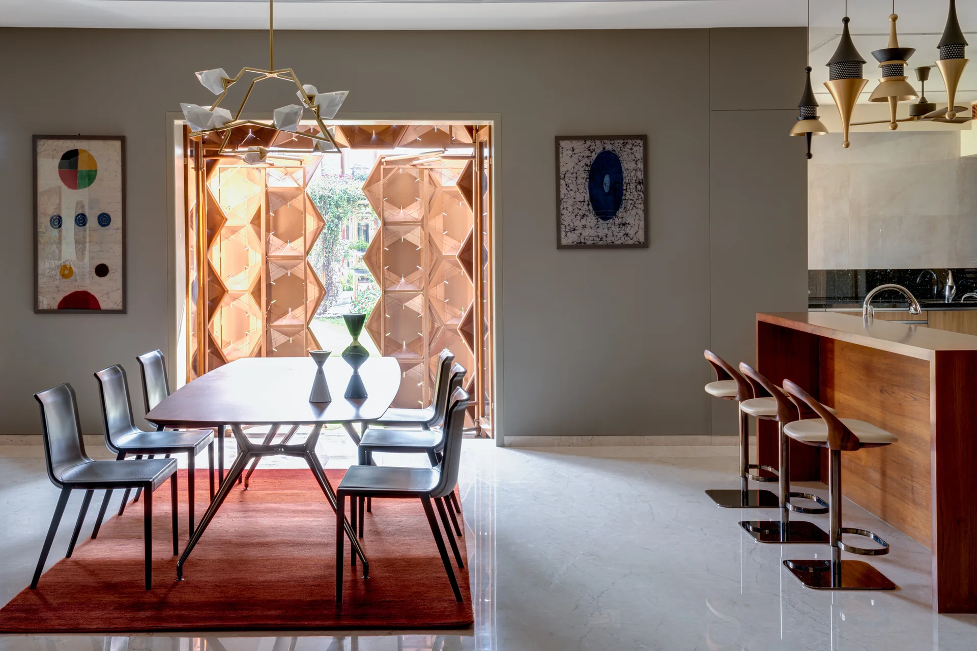 A modern dining room features a wooden table, dark chairs, and a terracotta rug next to a bar counter and geometric folding doors.