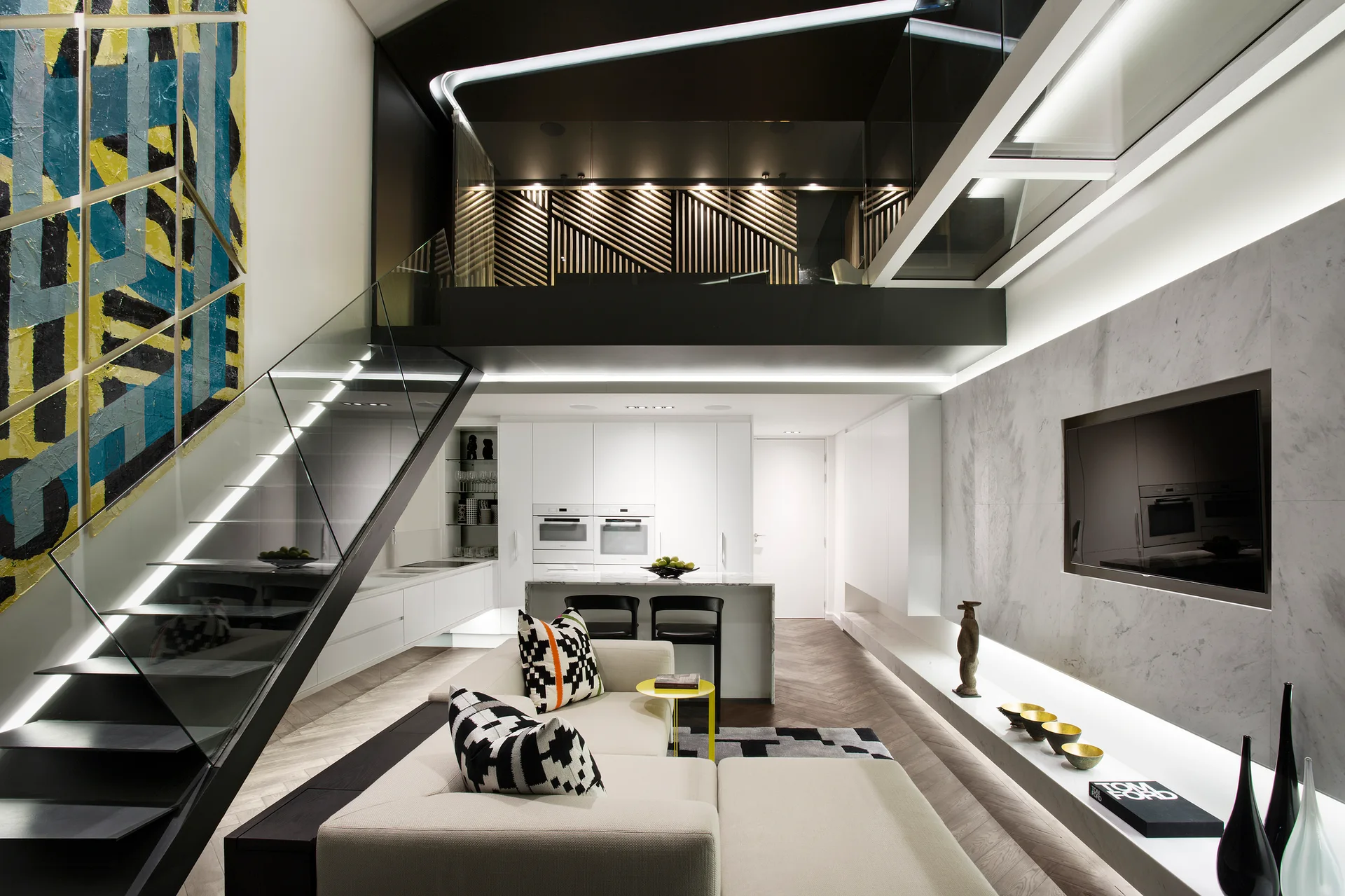 A contemporary open-plan living room features a black floating staircase with glass railings leading to a mezzanine level above a white kitchen.