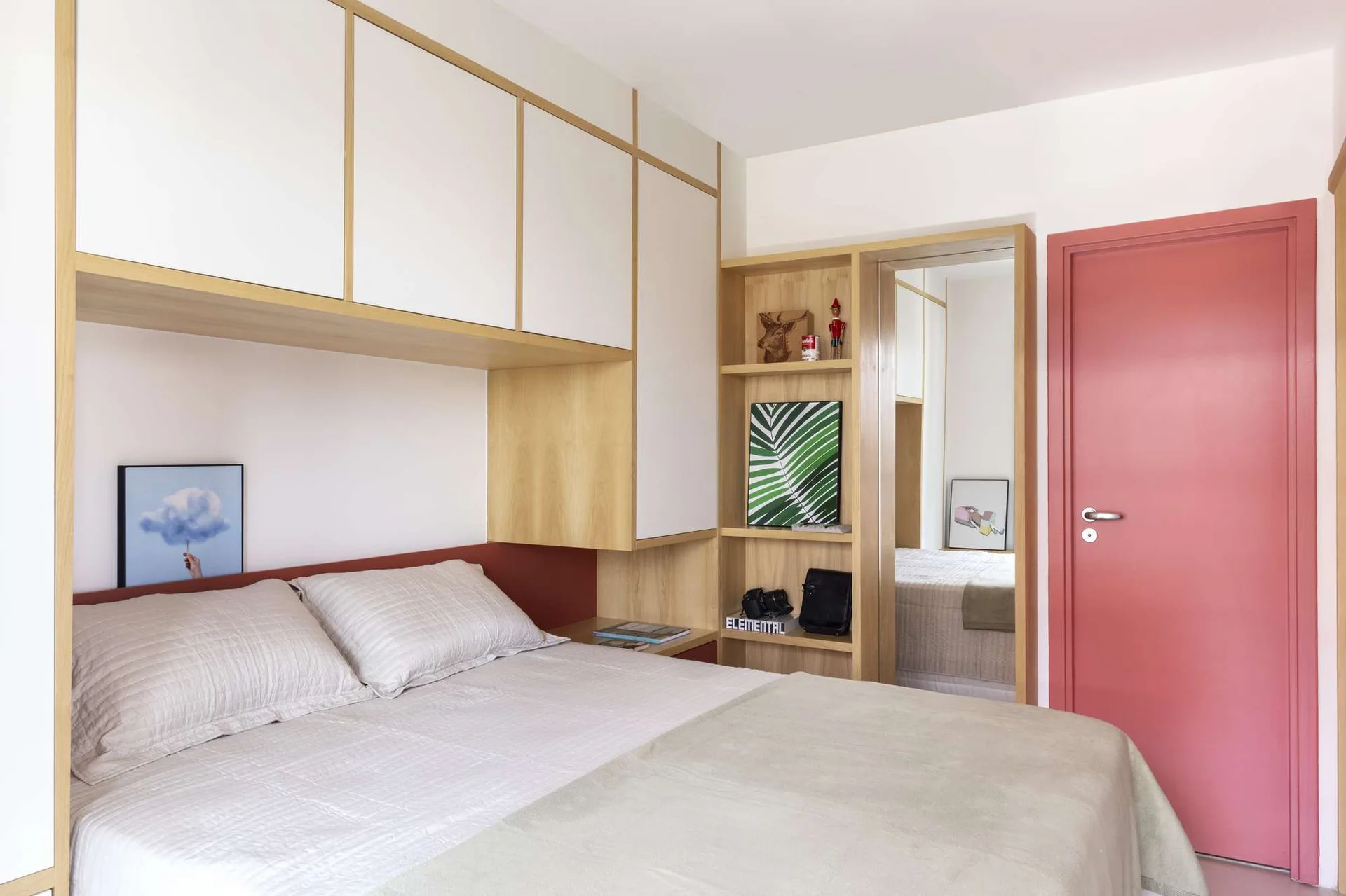 A minimalist bedroom features a bed tucked beneath custom wood and white overhead cabinets next to built-in shelves and a dusty pink door.