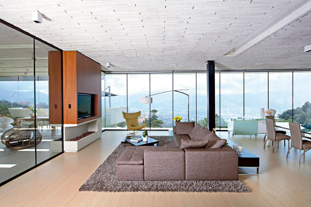 A modern living room features a brown sectional sofa, a yellow armchair, and floor-to-ceiling windows showcasing a panoramic mountain view.