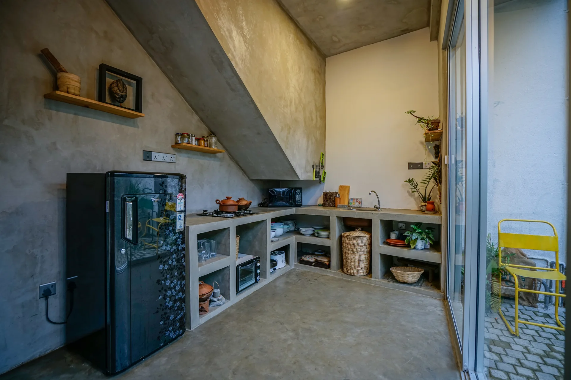 A minimalist grey concrete kitchen features cast-in-place countertops with open storage cubbies beneath a slanted concrete ceiling.
