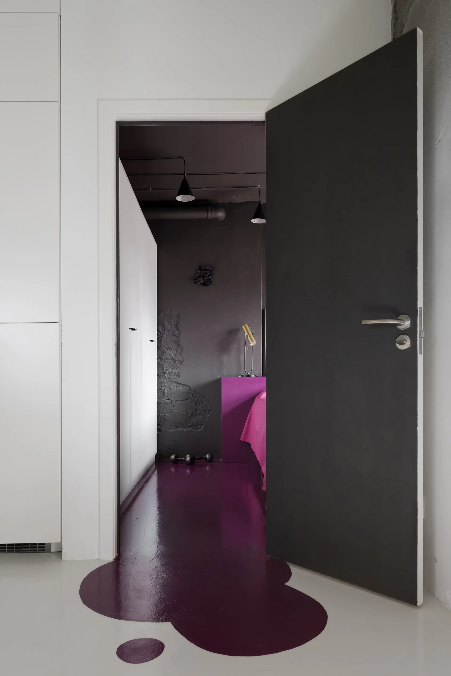 A view through an open dark gray door into a bedroom featuring dark walls, a white wardrobe, and a glossy purple floor that spills into the hallway.