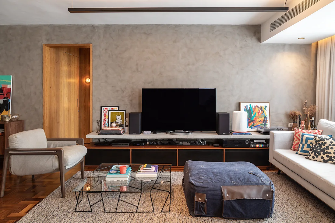 A living room featuring a concrete media console under a television, set against a textured grey plaster wall next to a wooden doorway.