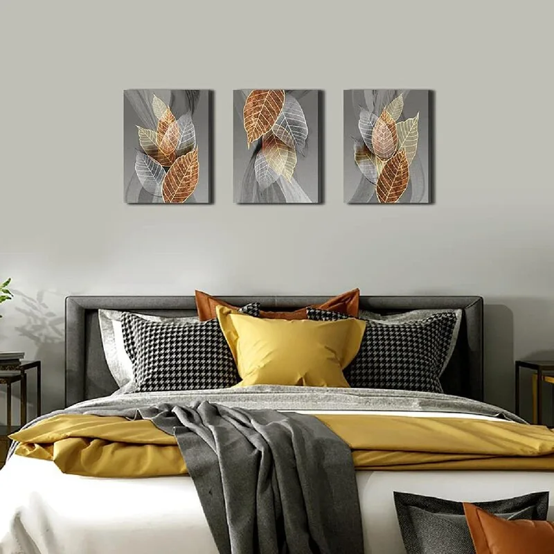 A grey bedroom featuring a dark headboard, mustard yellow and houndstooth pillows, and three framed leaf canvases hanging symmetrically on the wall.