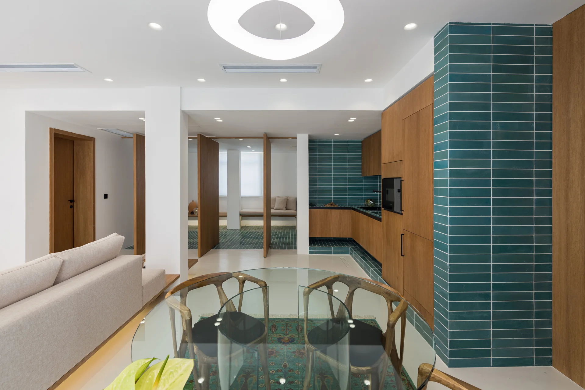 An open kitchen and dining space featuring wood cabinets, a teal tiled wall accent, wooden partition screens, and a round glass table.