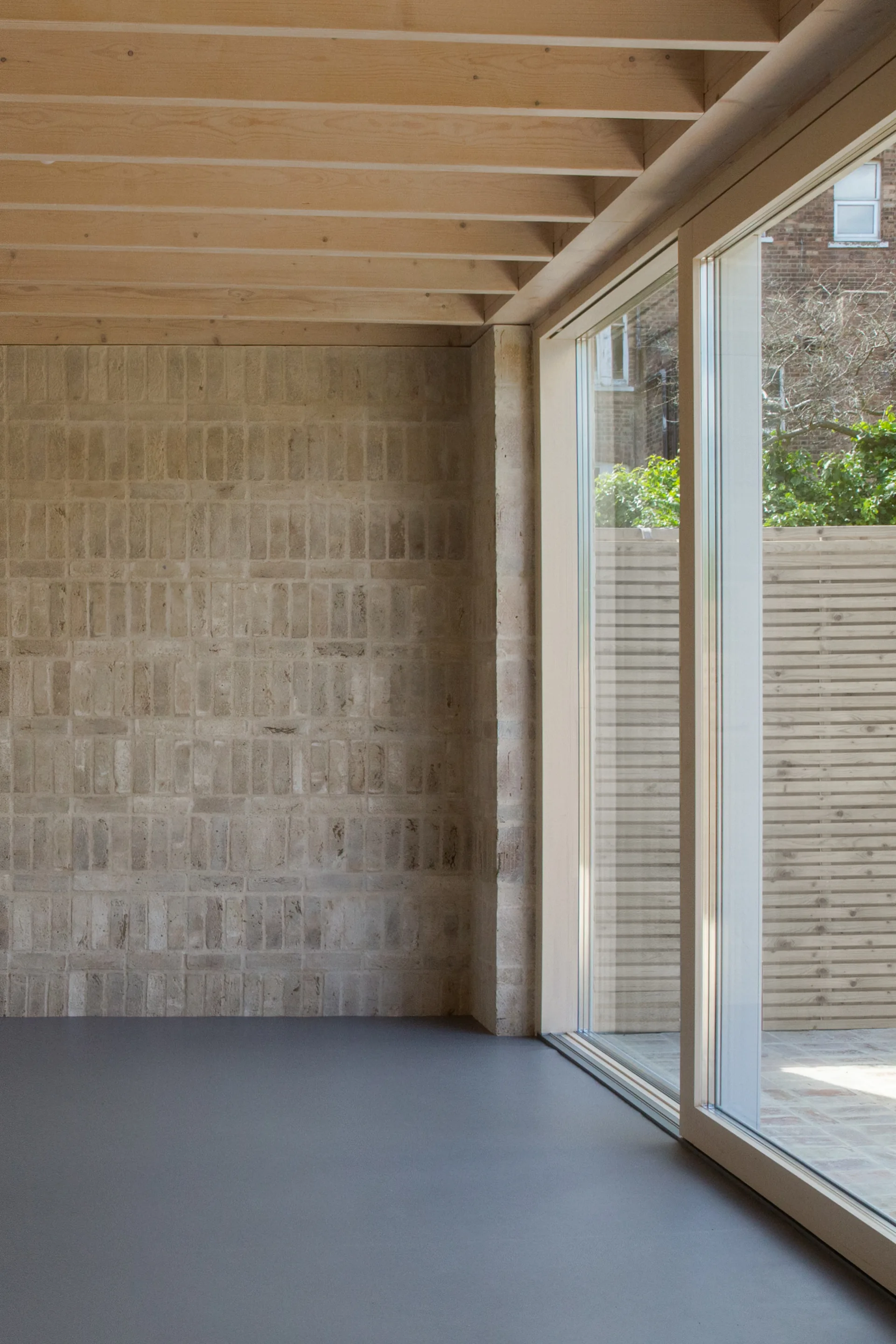 An empty room features an exposed light wood joist ceiling, a textured beige brick wall, and a large sliding glass door opening to a patio.