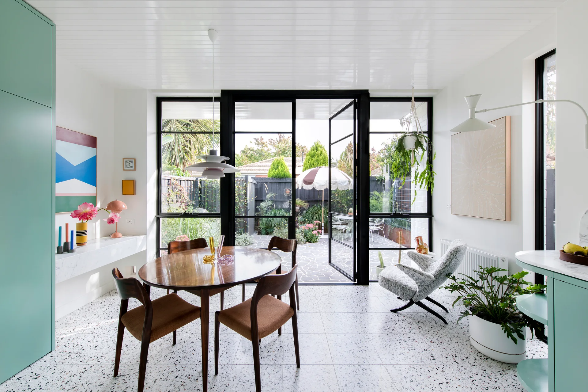 A bright dining area features a wood table, mint green built-in cabinets, and a black-framed glass door opening to a garden.